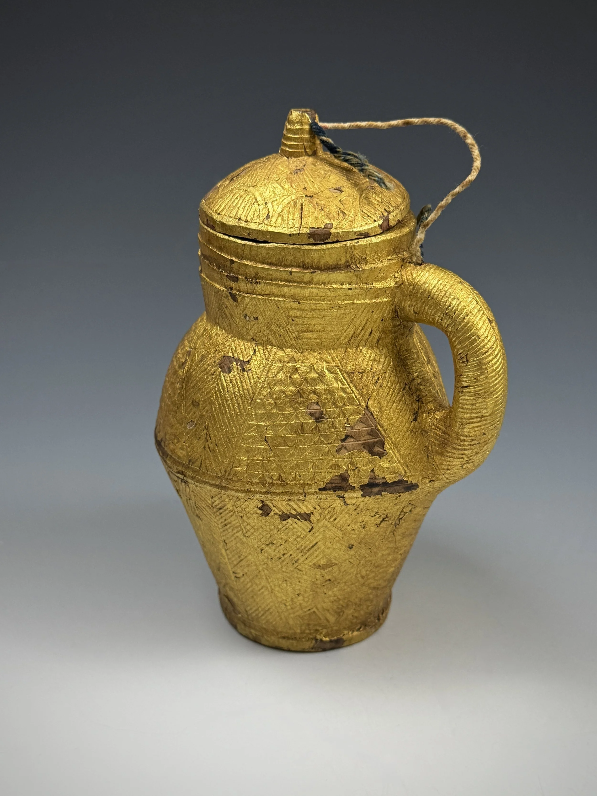 A Baule prestige object. This miniature wood carving covered with gold foil is a functional representation of a ceramic lidded vessel with intricate carved designs throughout the surface of the container. 16cm H. Ex Galarie Noir d'Ivoire, Paris, Ex