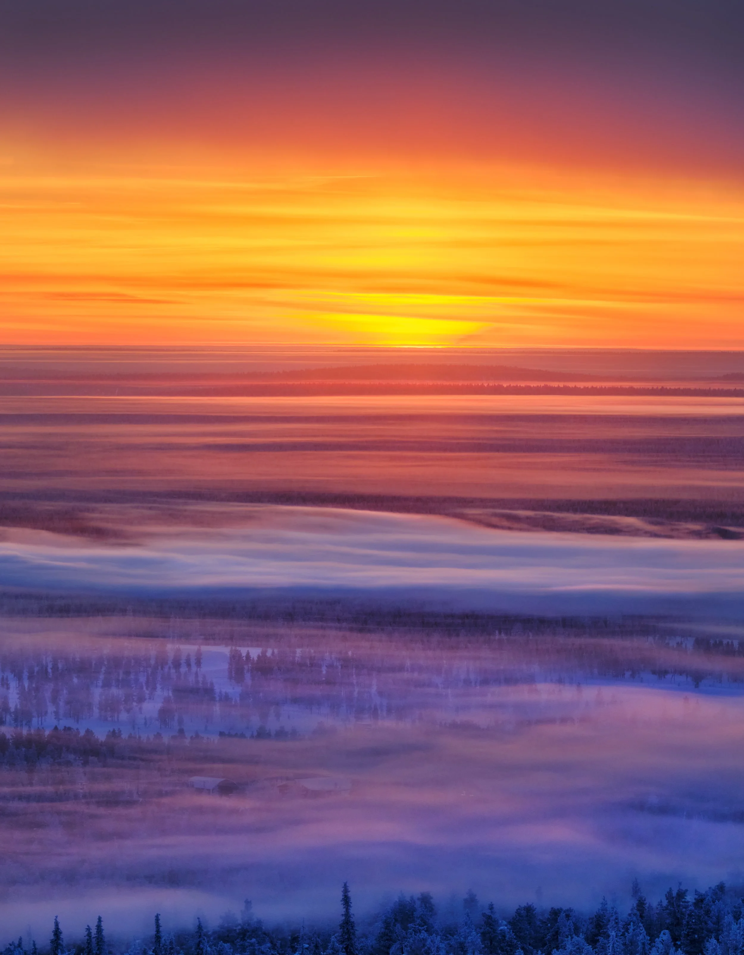 Colorful sunset over a snow-covered landscape with trees and fog.