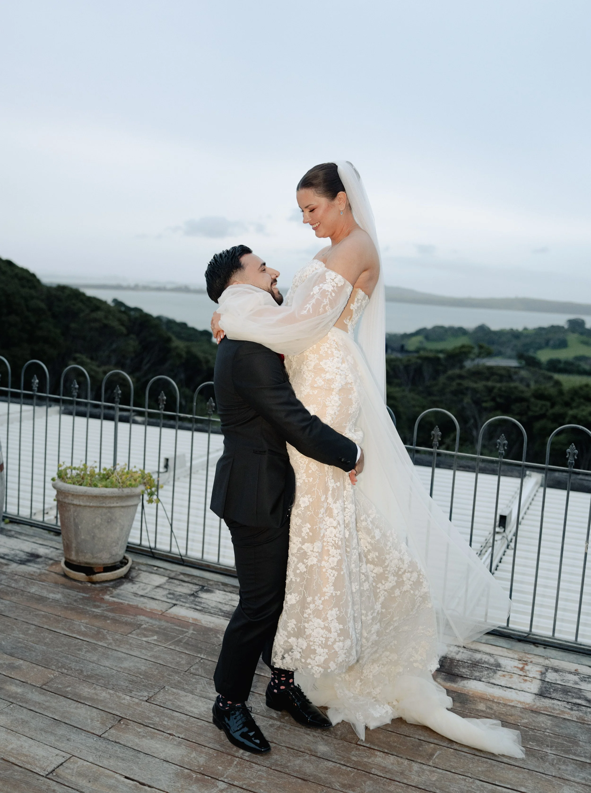 Bride and groom on a rooftop, with the groom lifting the bride, outdoors at sunset.
