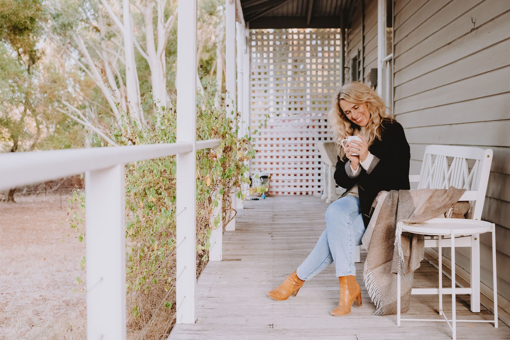 A woman sits on the Shepherds Hill Cottage verandah, holding a mug of coffee