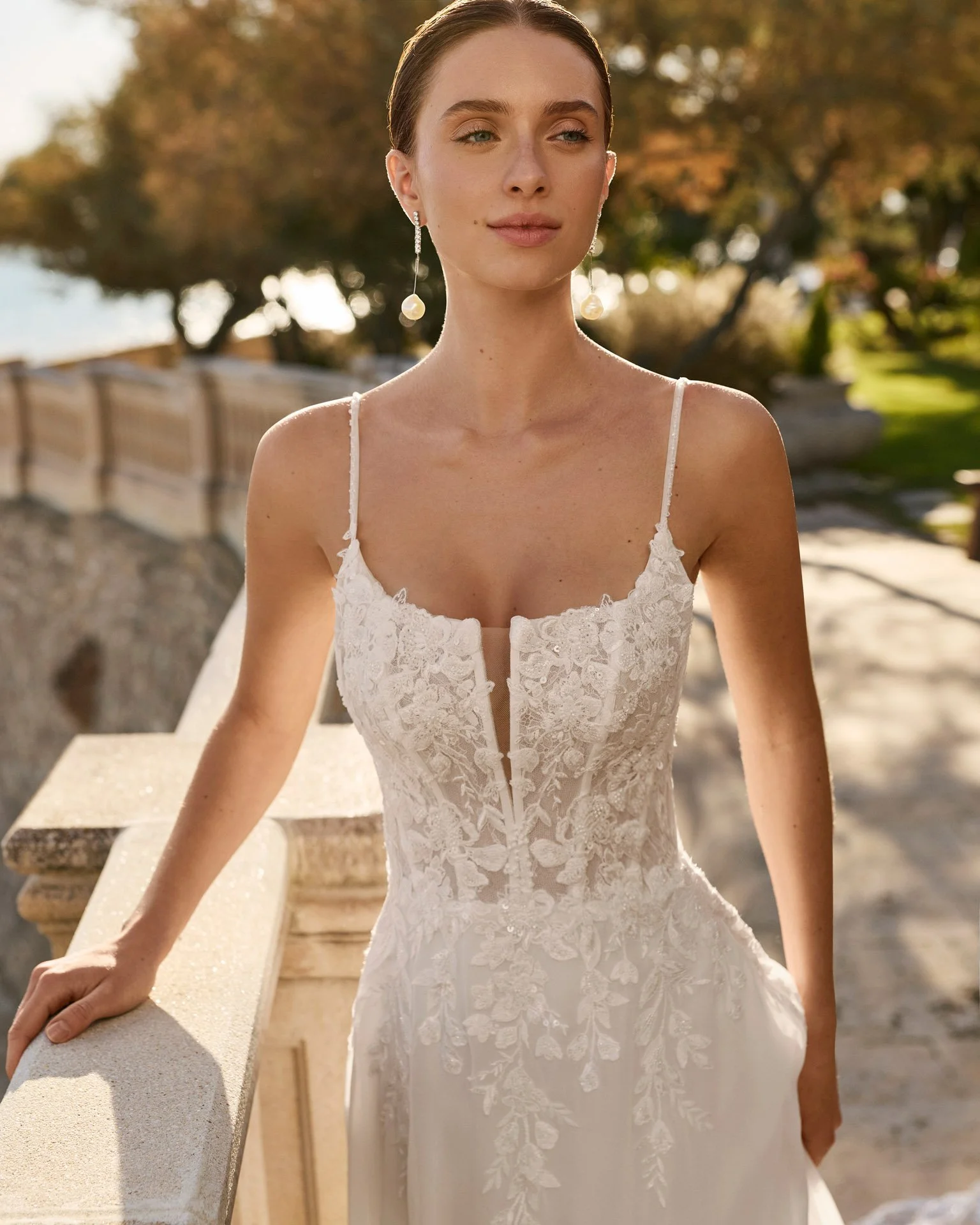 Vestido de noiva Feneya com corpete estruturado em rendas delicadas e pequena pedraria, cintura definida e decote quadrado com V profundo no peito.