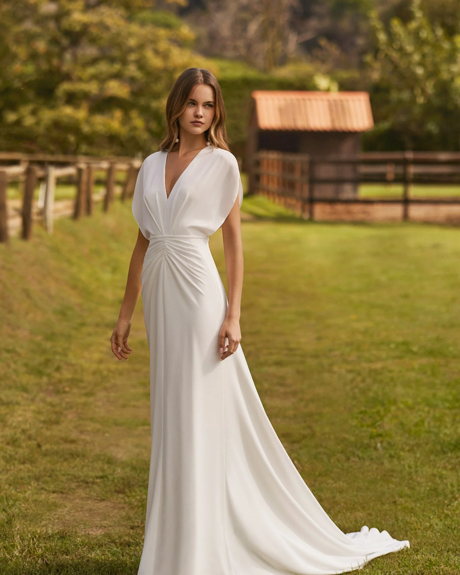 Vestido de noiva sereia Nairol em crepe, com decote em V, corpete drapeado, mangas borboleta e delicado cinto de pedraria.