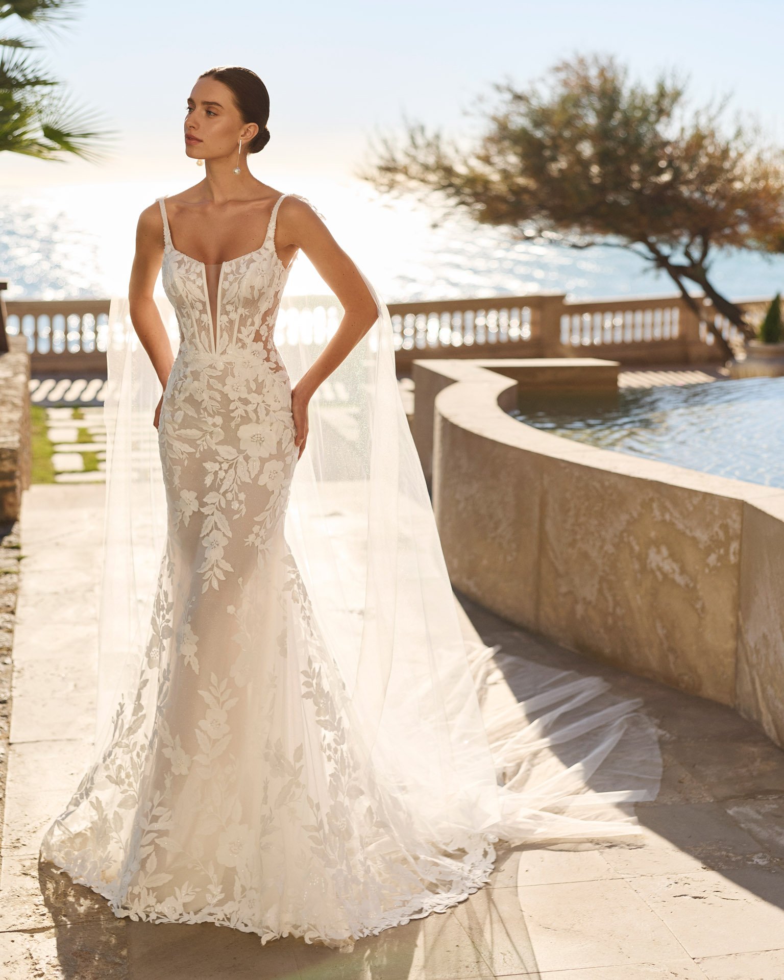 Vestido de noiva Fibula de corte sereia, totalmente rendado, com corset, decote em V profundo, transparências laterais e alças finas em pedraria.