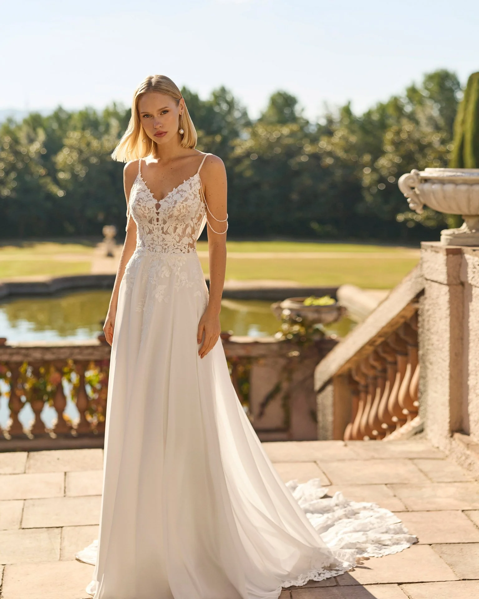 Vestido de noiva Felisa de corte esvoaçante em chiffon, com corpete em rendas delicadas, decote em V, alças finas em pedraria e detalhes de pedraria sobre os ombros.