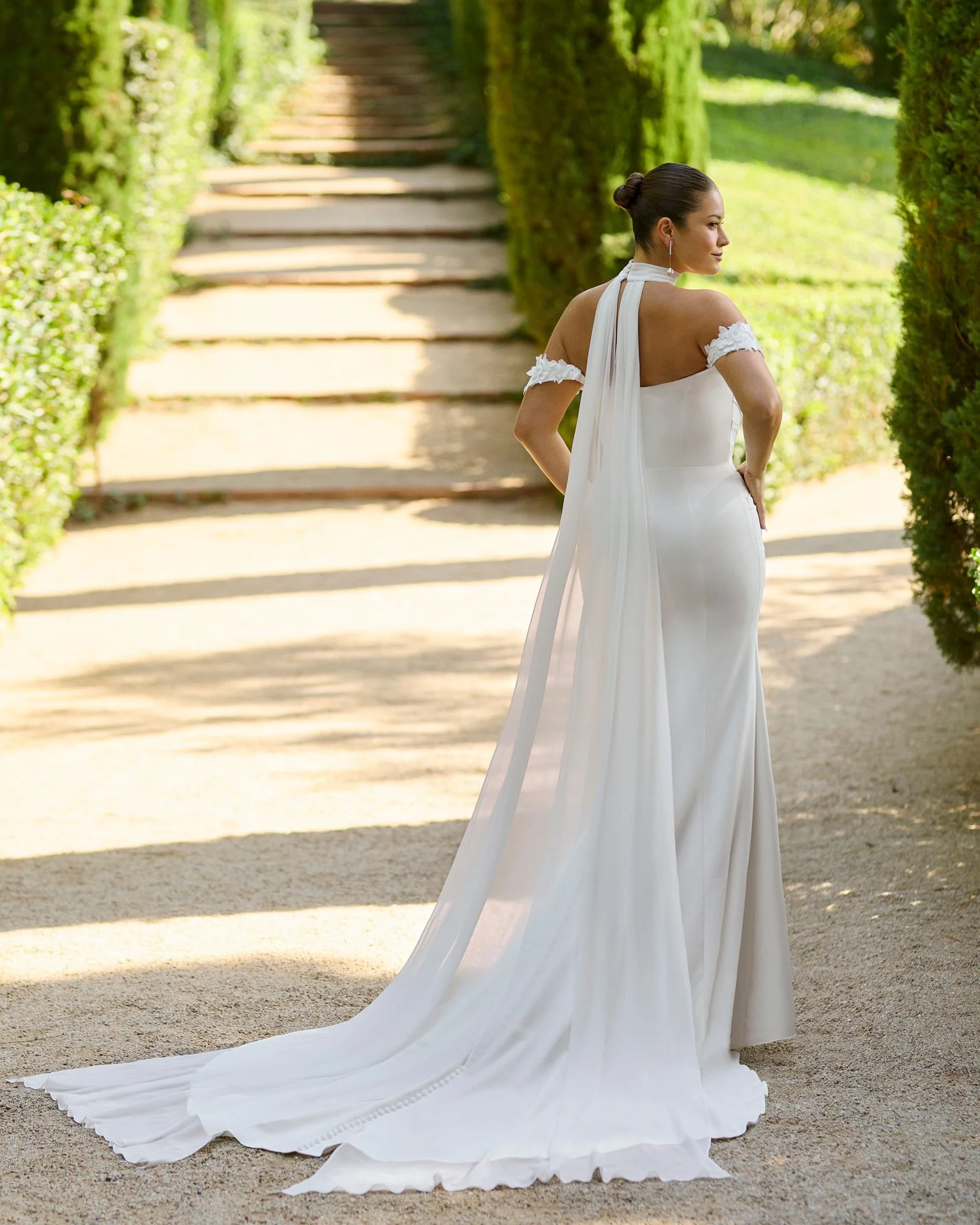 Vestido de noiva Kairy em crepe com alças caídas e gargantilha removível em chiffon, da qual partem duas capas longas nas costas.