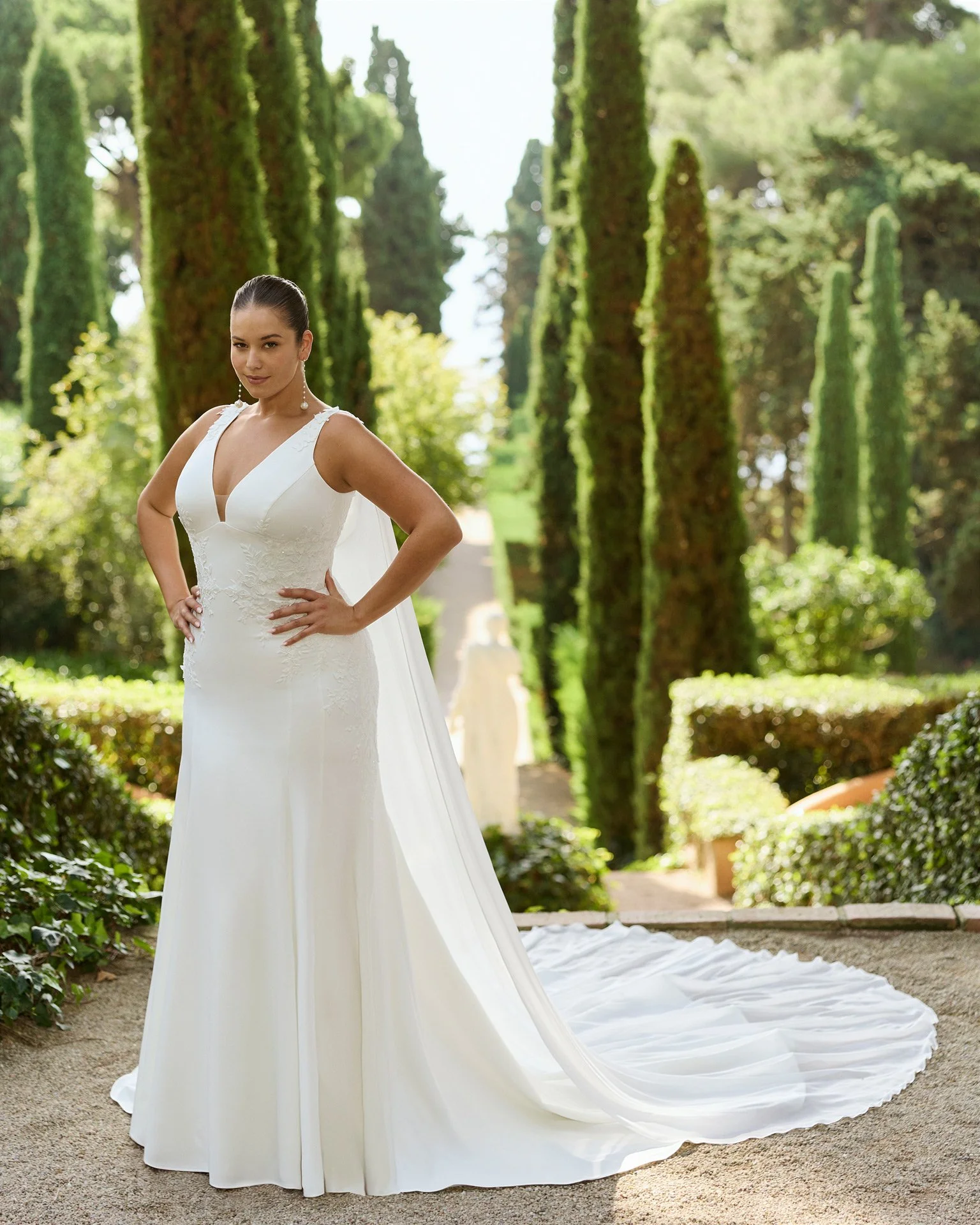 Vestido de noiva sereia Kamara em crepe estruturado, com decote em V profundo, alças largas e detalhe em renda a definir a cintura.