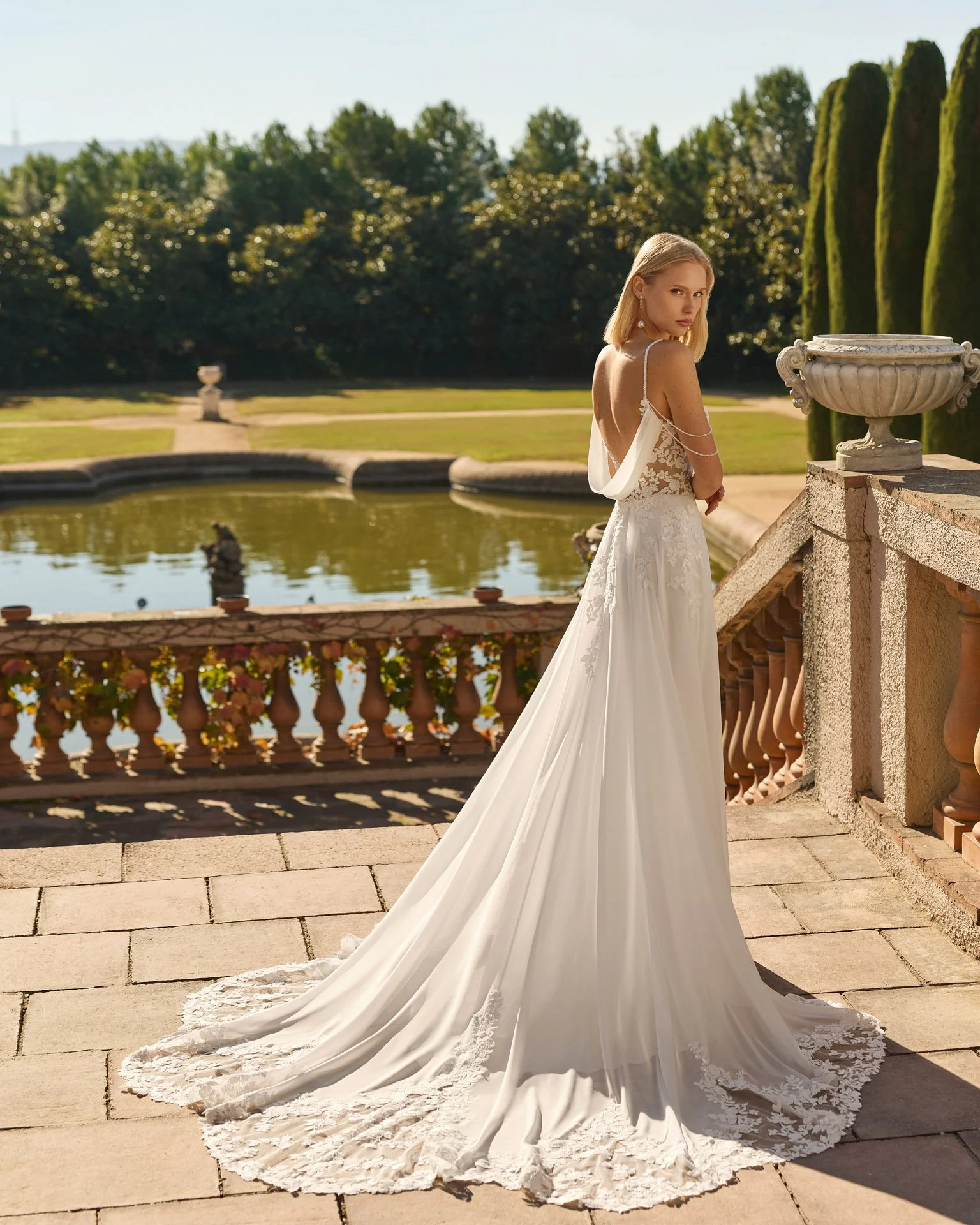 Vestido de noiva Felisa em chiffon, com decote em V profundo nas costas emoldurado por uma capa subtil, detalhes de pedraria nos ombros e cauda rendada.