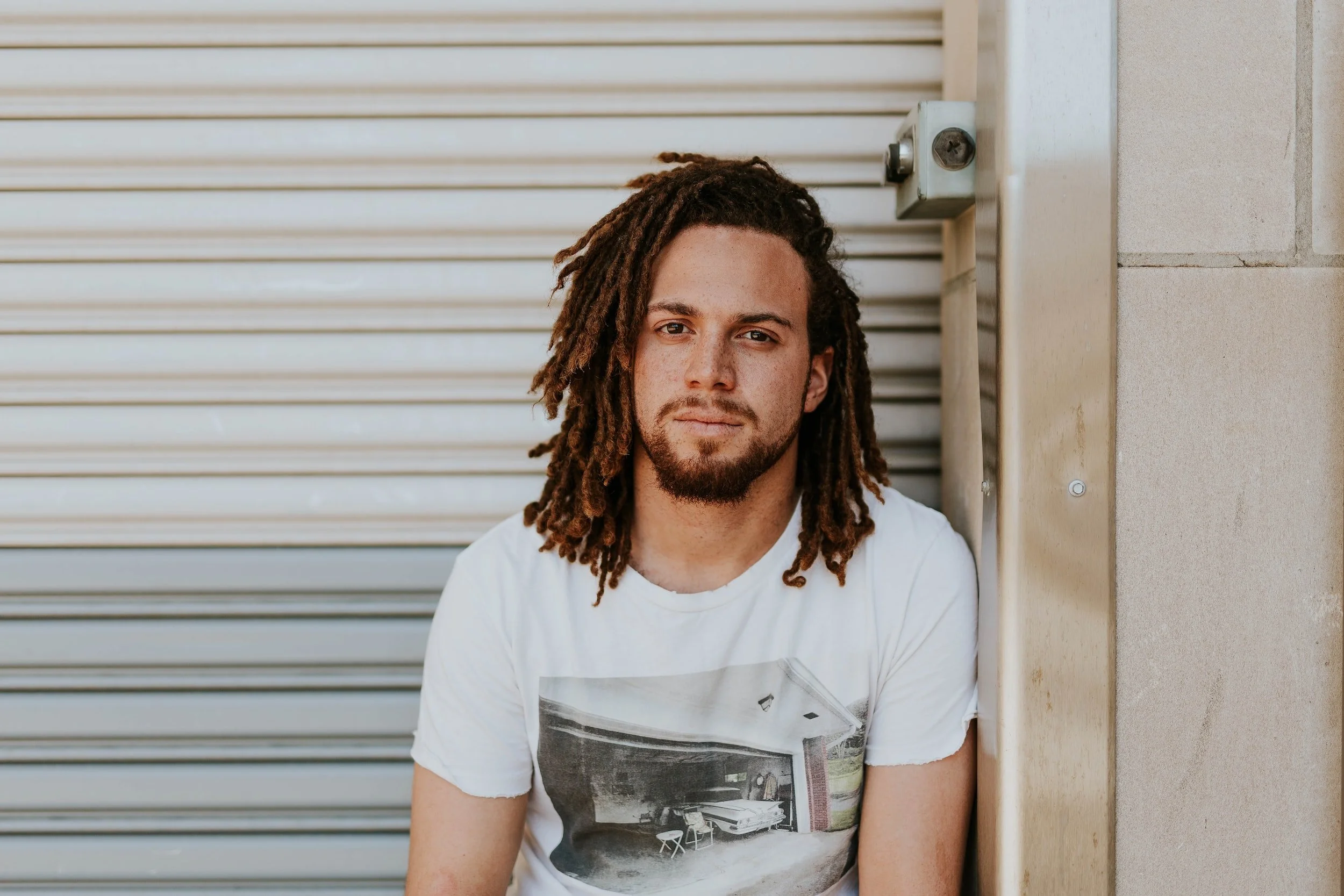 Man with dreads leaning against garage by Brooke Cagle