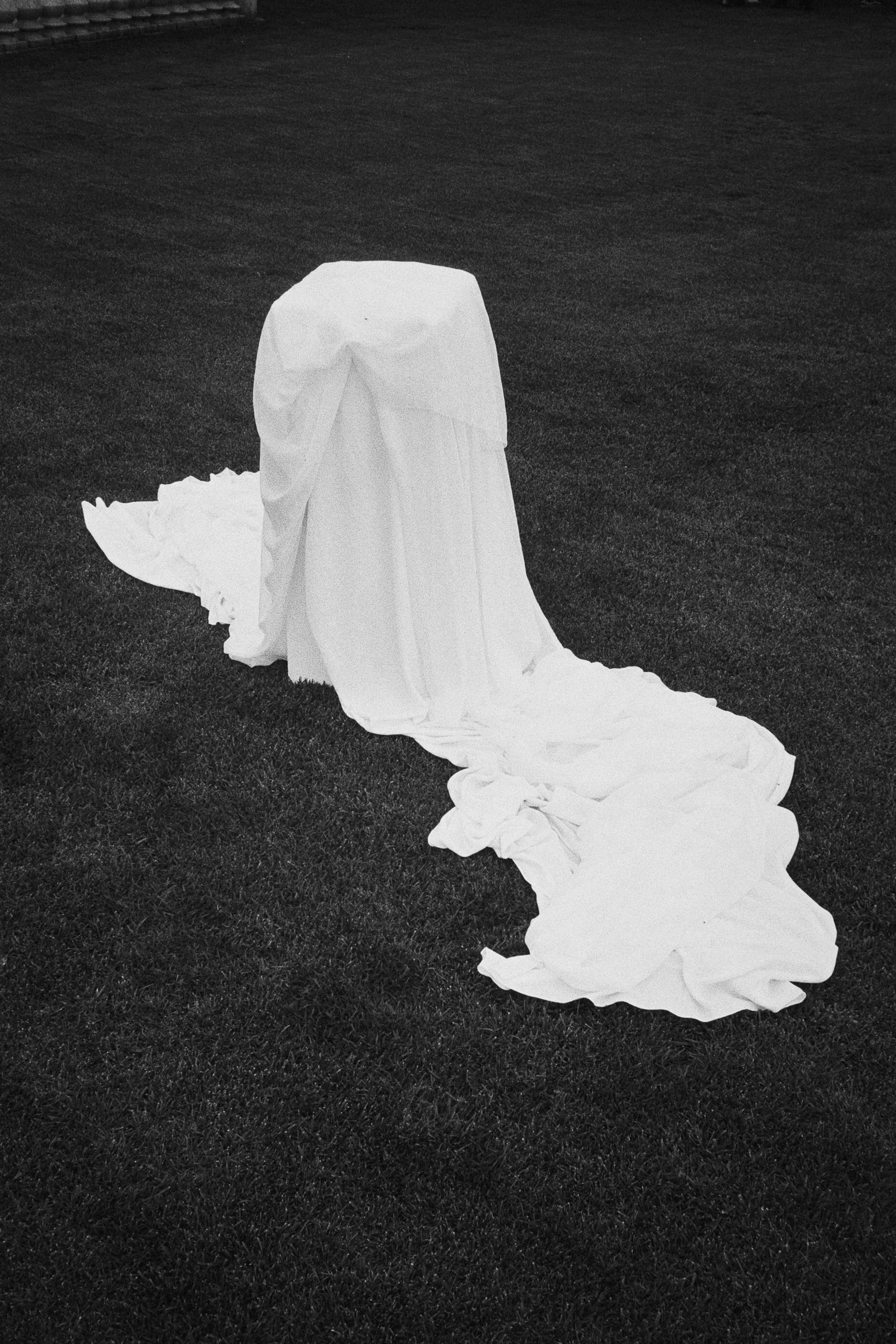 A long piece of white fabric or paper draped on grass, with a portion gathered and flowing on the ground.