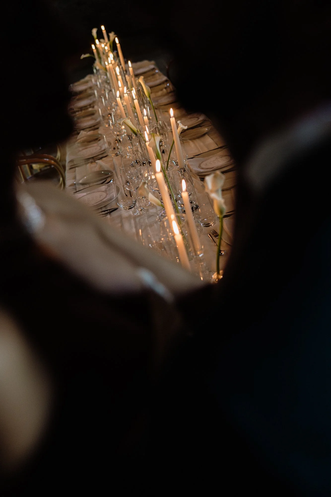 A table set with lit candles, glassware, and napkins, viewed through a narrow opening.
