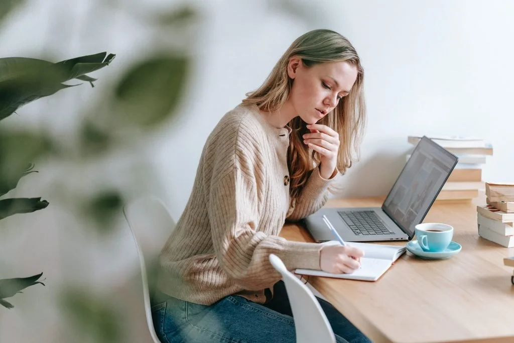 corporate-casual-woman-writing-laptop-coffee-table-plant
