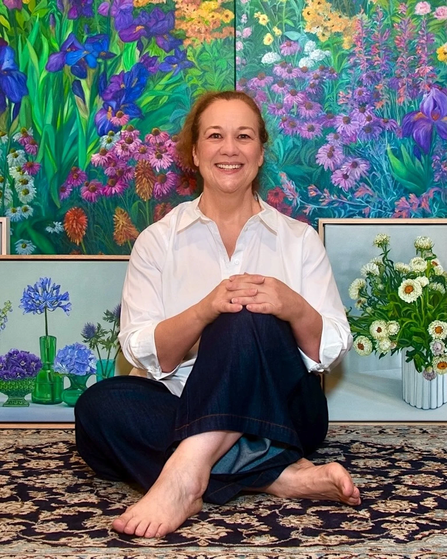 Robyn Markey sitting on carpet in front of her original floral oil paintings