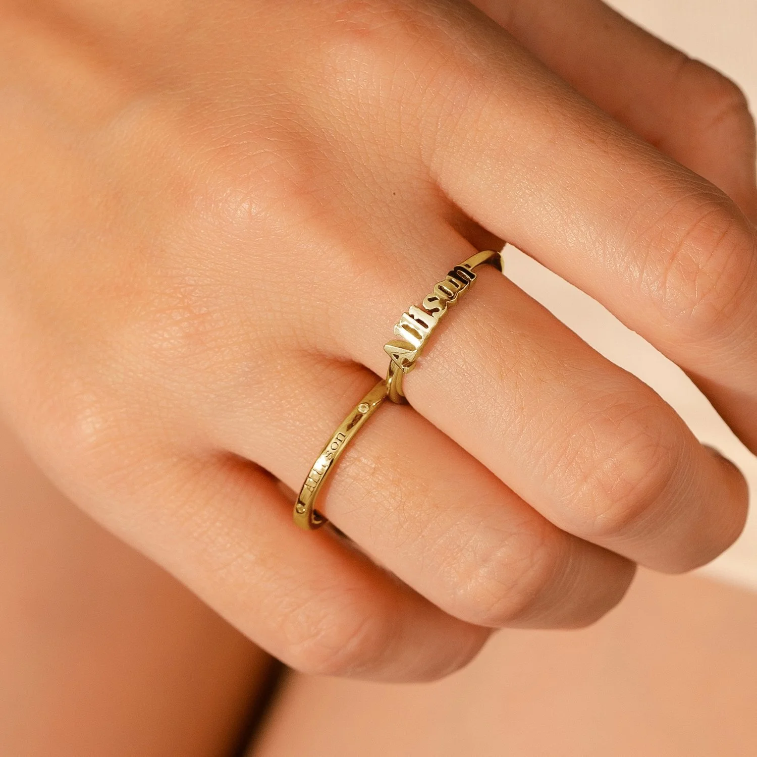 Close-up of a person's hand wearing two gold rings with engraved text.