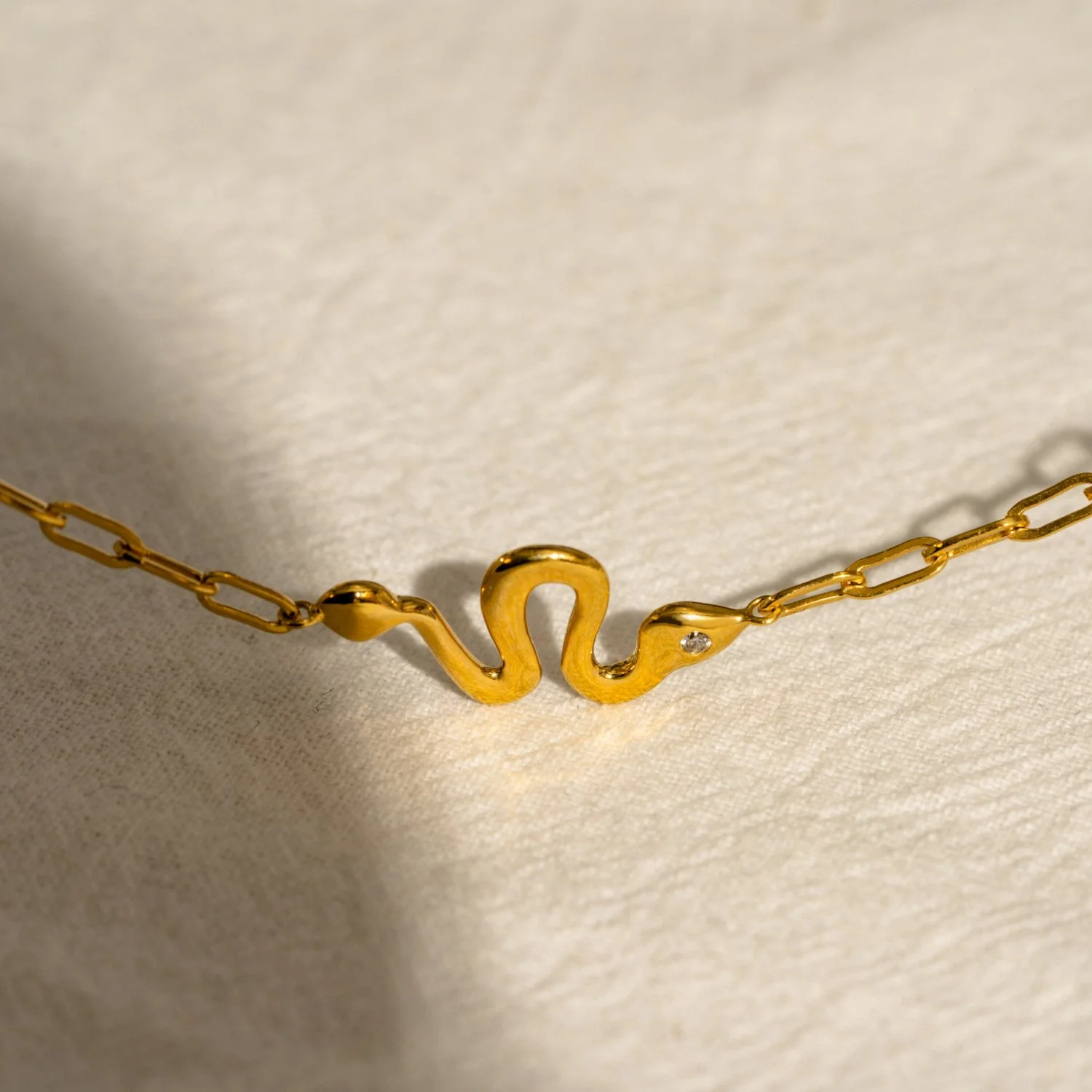 Gold necklace with a pendant of two swans facing each other, connected at the necks.