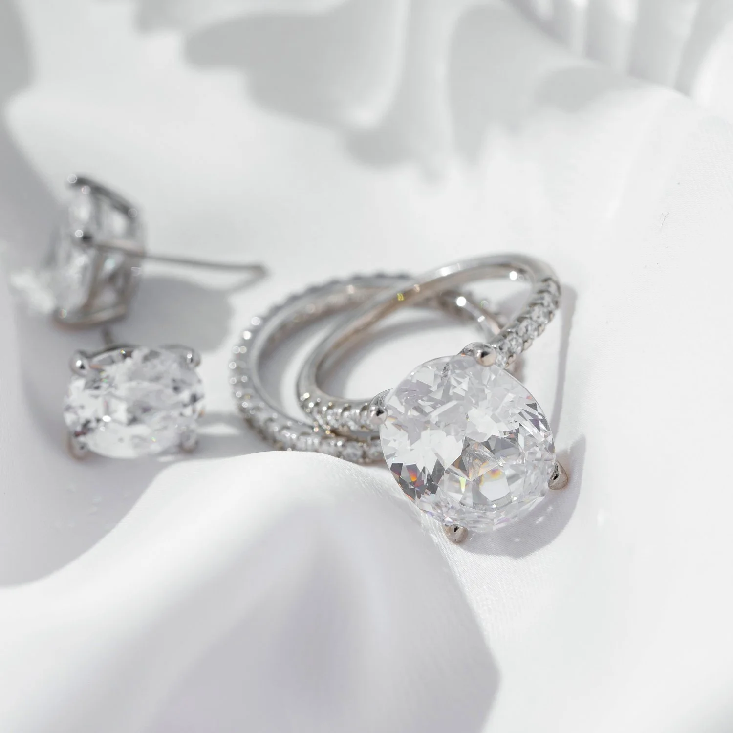 Silver jewelry including a large diamond ring, a smaller diamond ring, and a pair of diamond earrings on white fabric