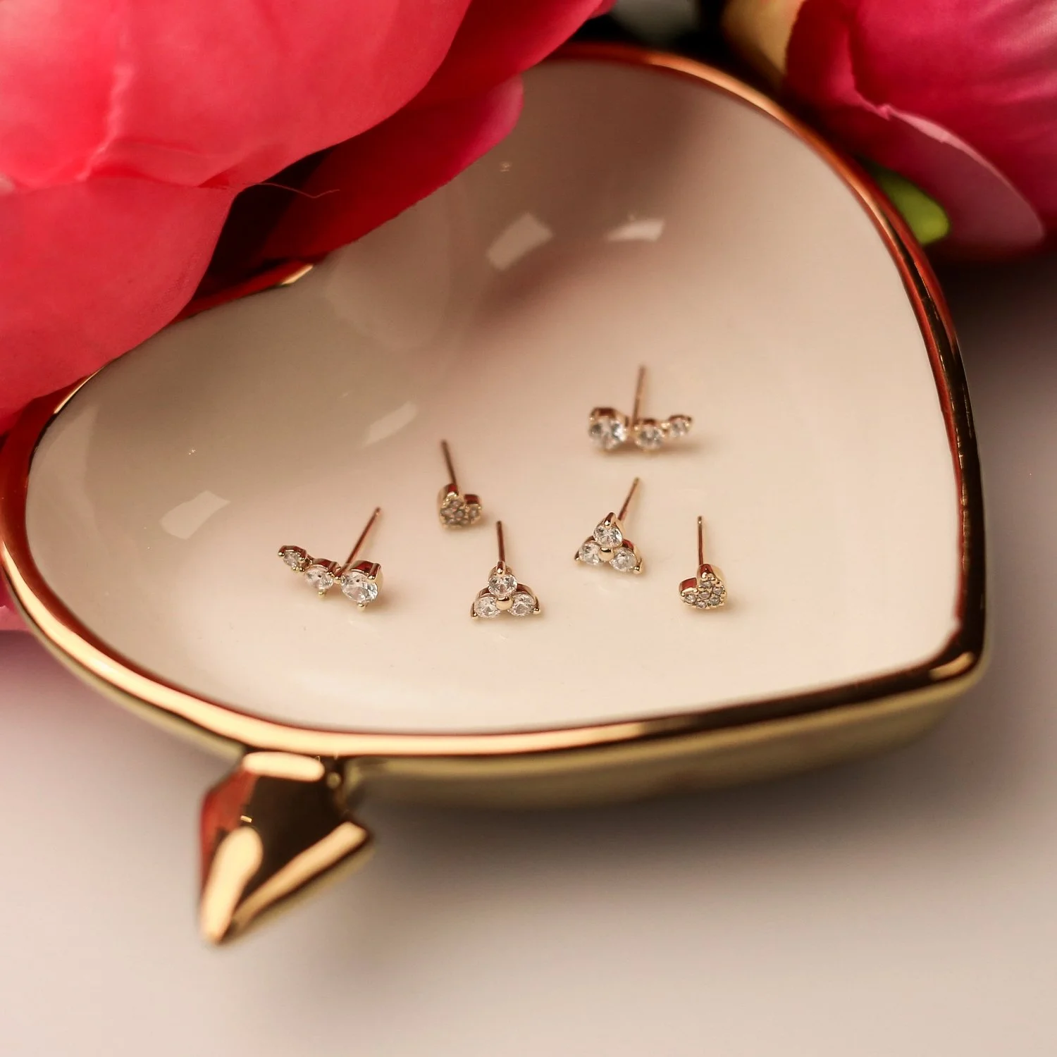 Heart-shaped jewelry box with six pairs of diamond earrings inside, surrounded by pink flower petals.