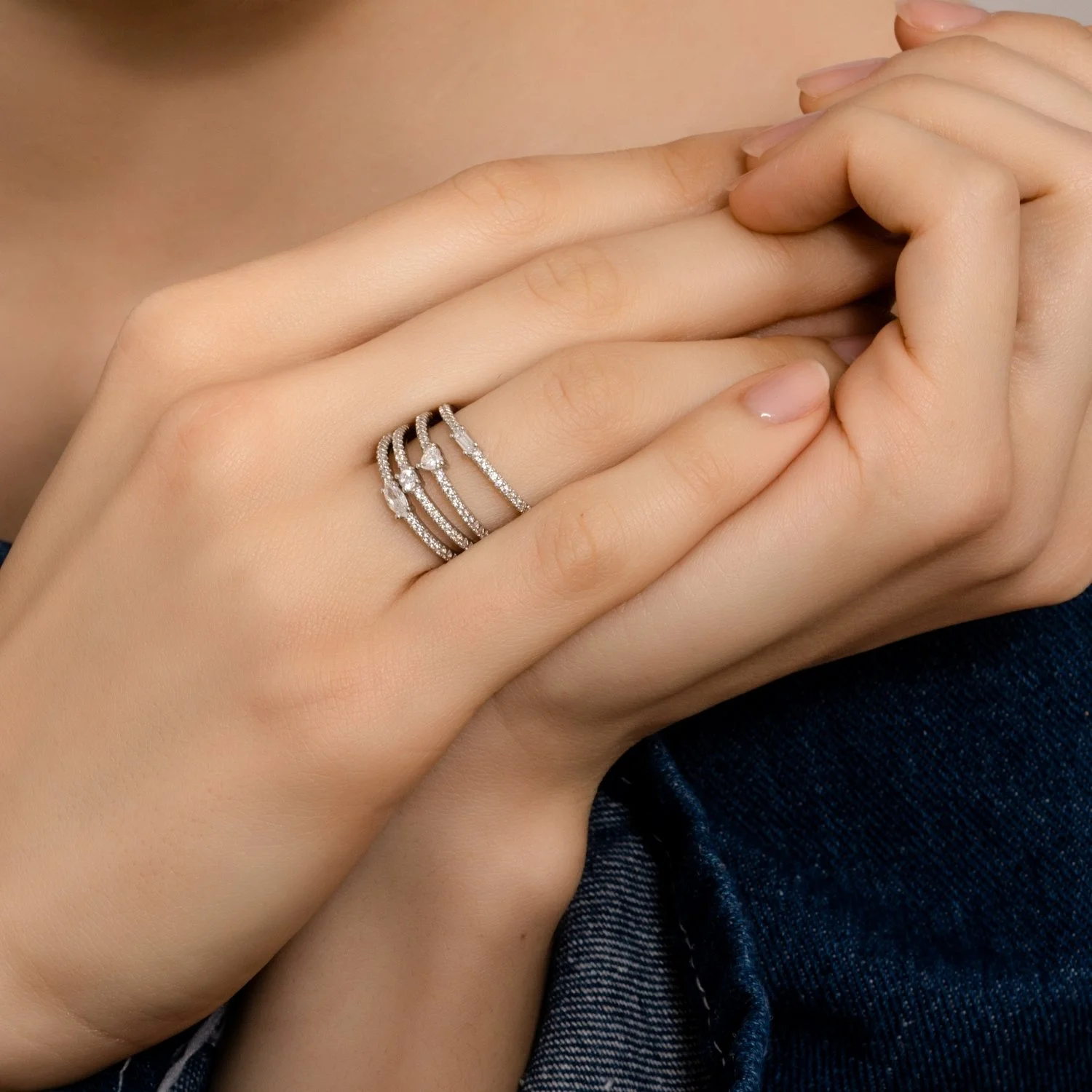 Close-up of a woman's hand with three diamond rings on her finger, holding her other hand.