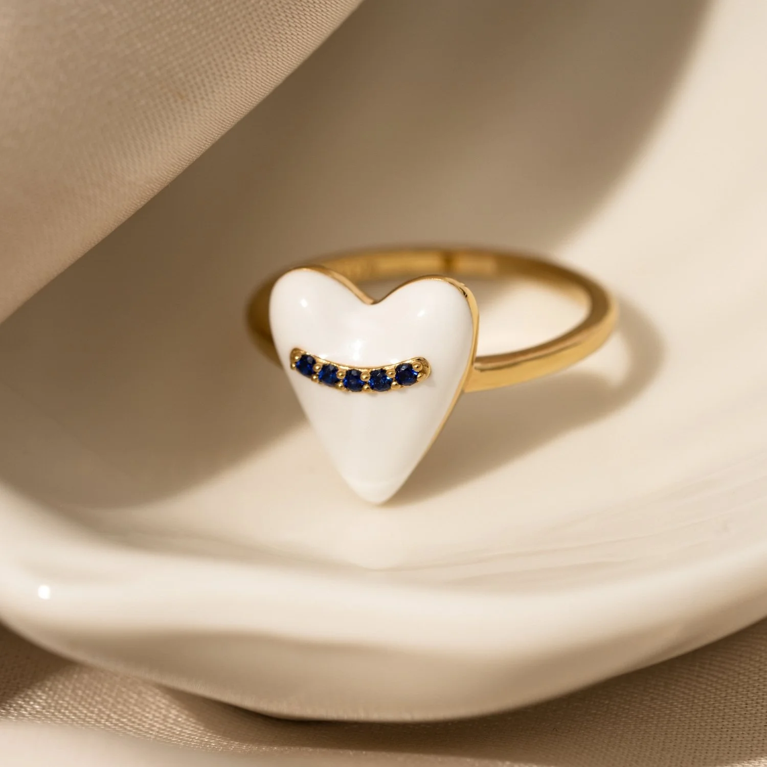 Gold ring with a white heart-shaped top and a row of small blue gemstones