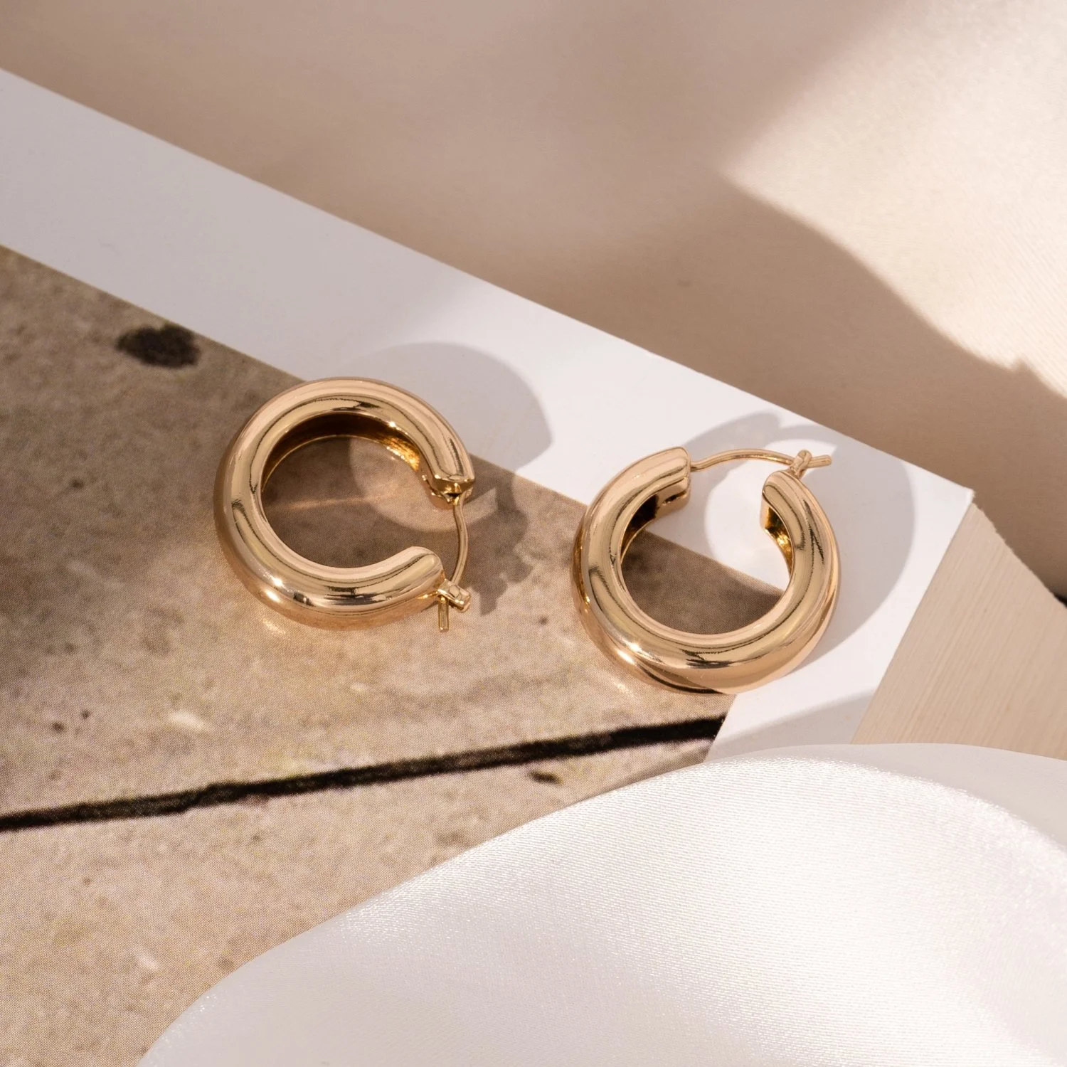 Pair of shiny gold hoop earrings placed on a rectangular mirror on a textured surface.