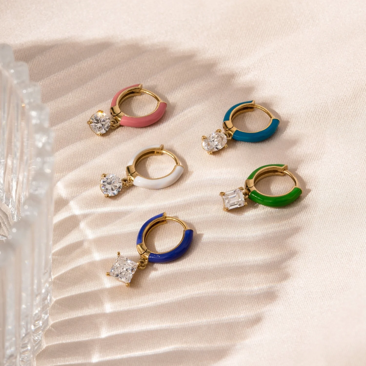 Colorful hoop earrings with gemstones on a beige satin surface.