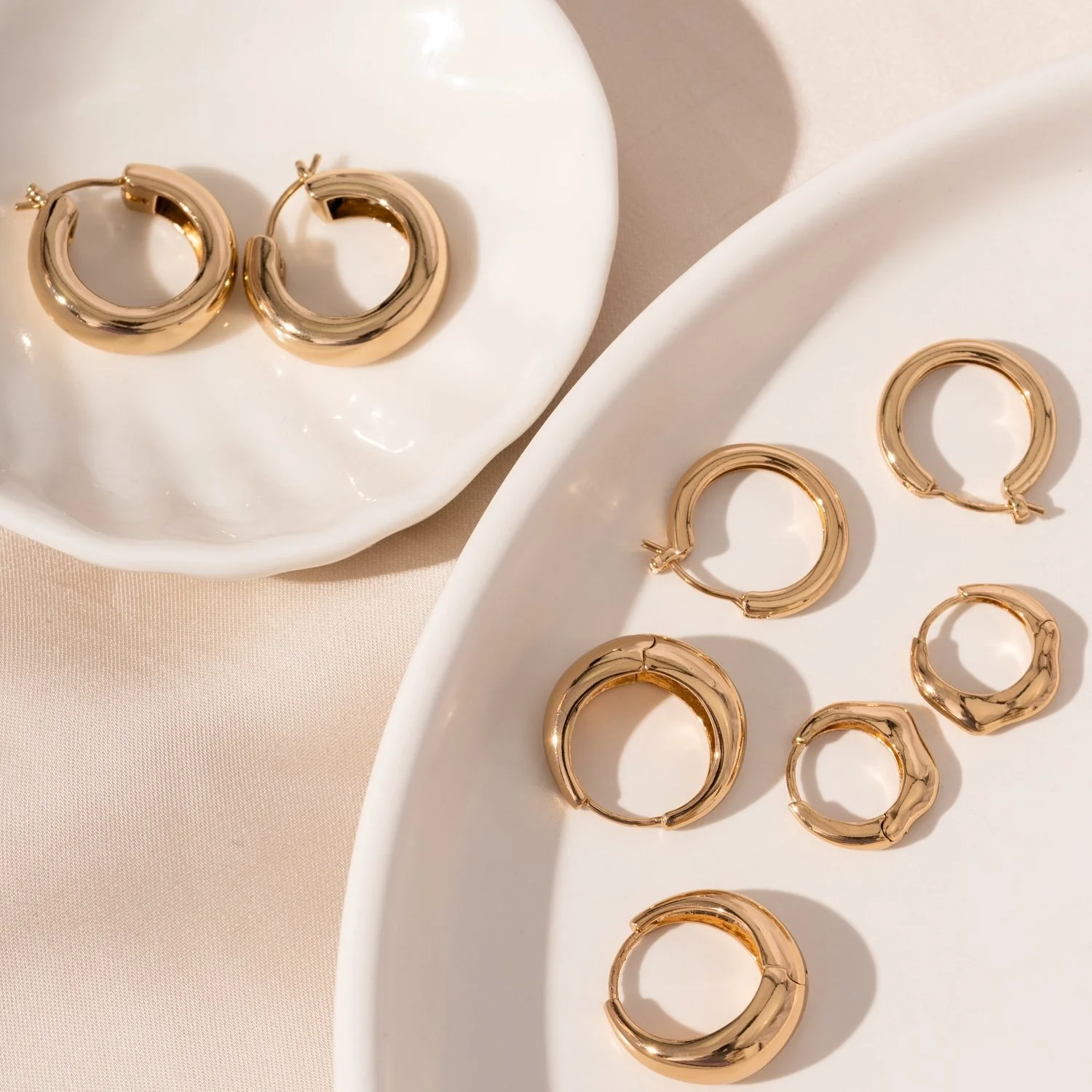Gold hoop earrings on white ceramic dishes with a neutral background.