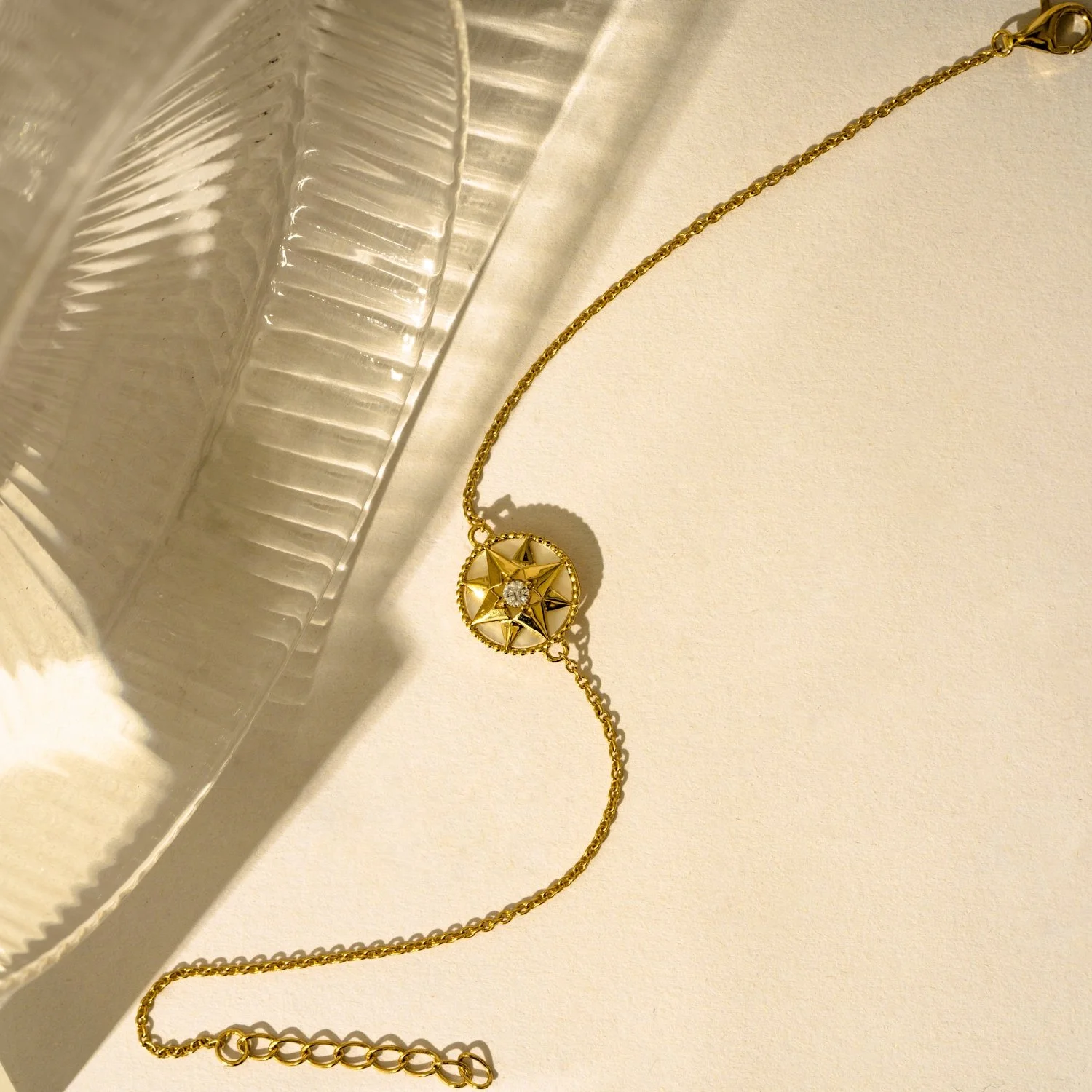 Gold necklace with a circular pendant featuring a star and a small gemstone, lying on a light-colored surface next to a reflective glass dish.