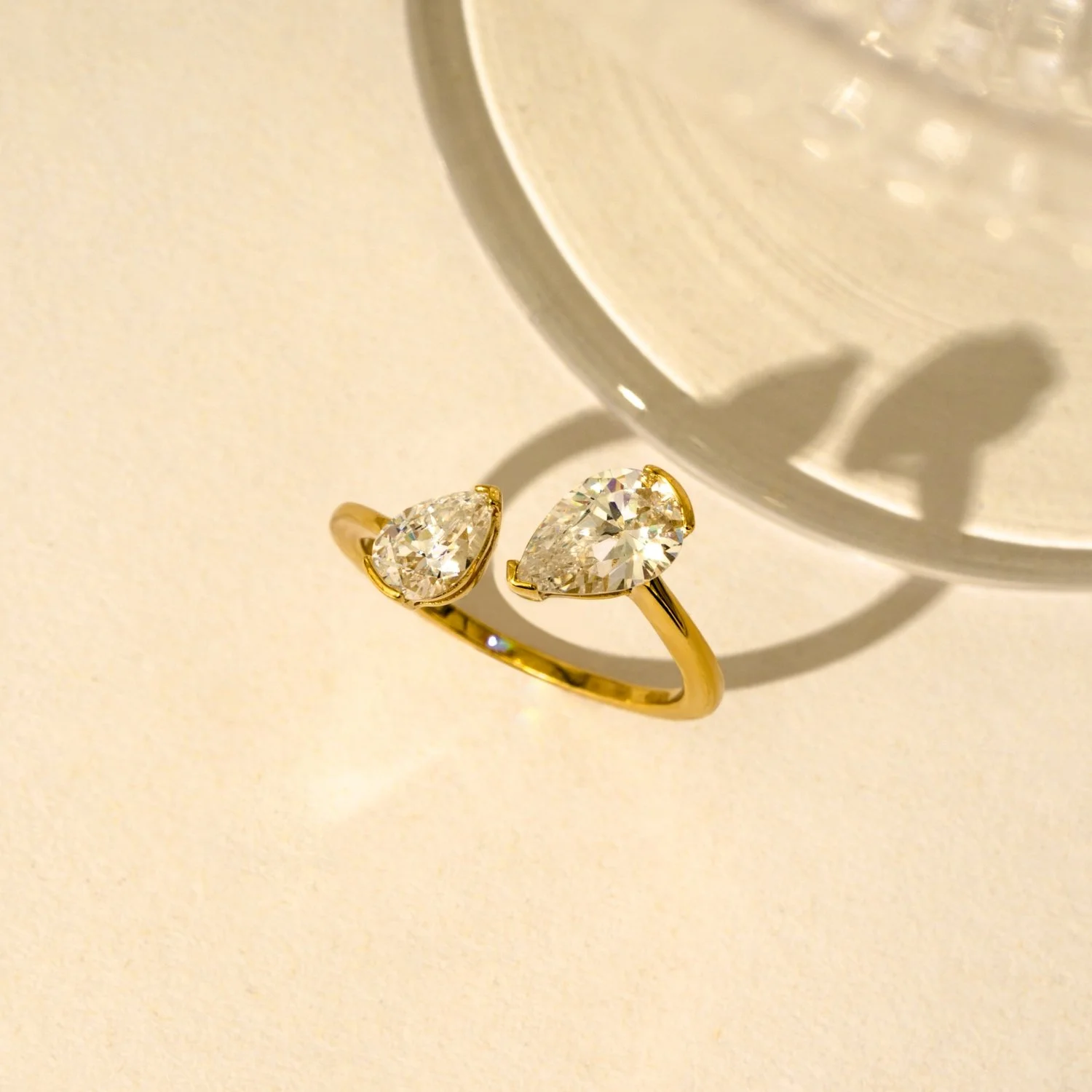 Gold ring with two large pear-shaped diamonds, resting on a white surface, casting a shadow beneath.