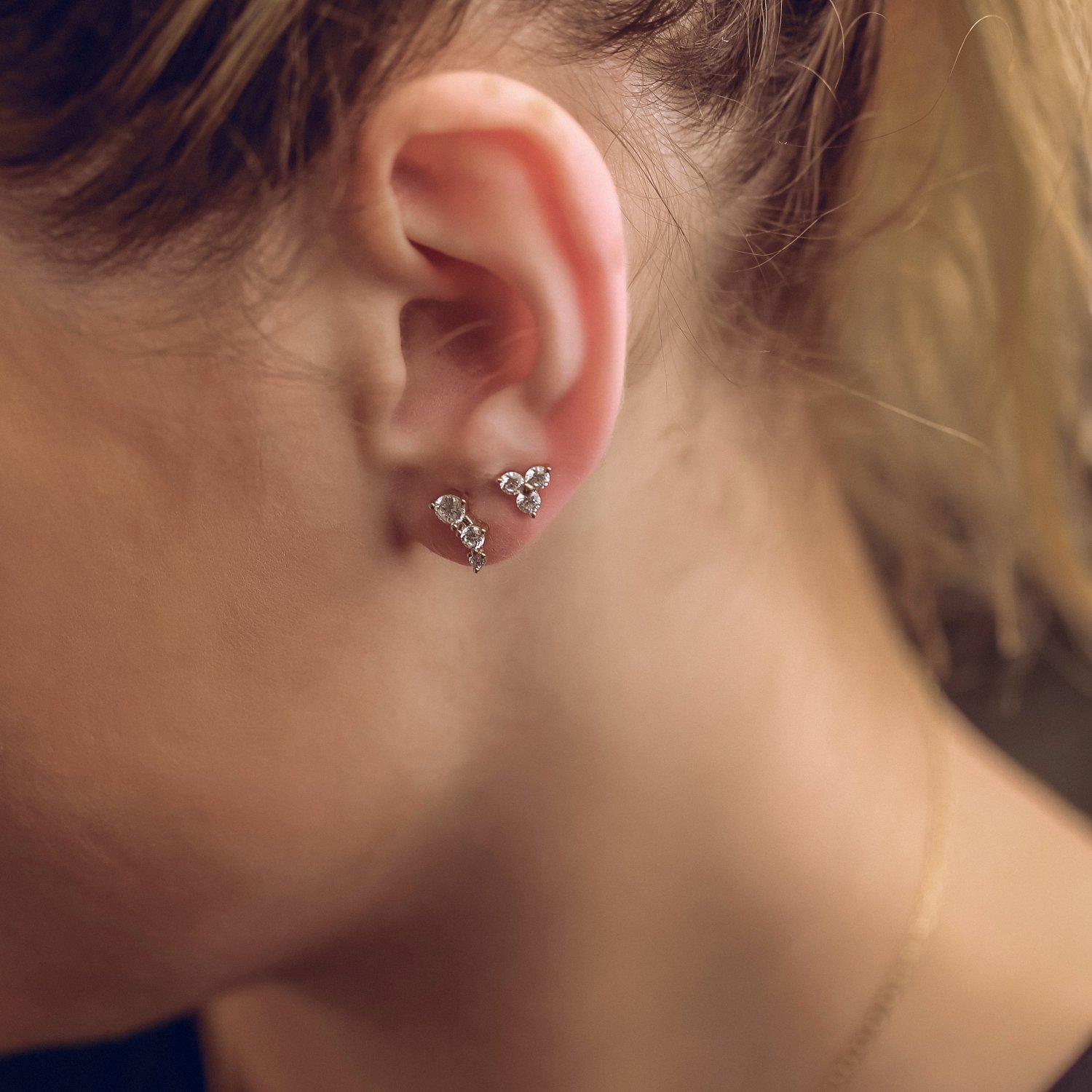 Close-up of a person's ear with three silver earrings adorned with small gemstones.