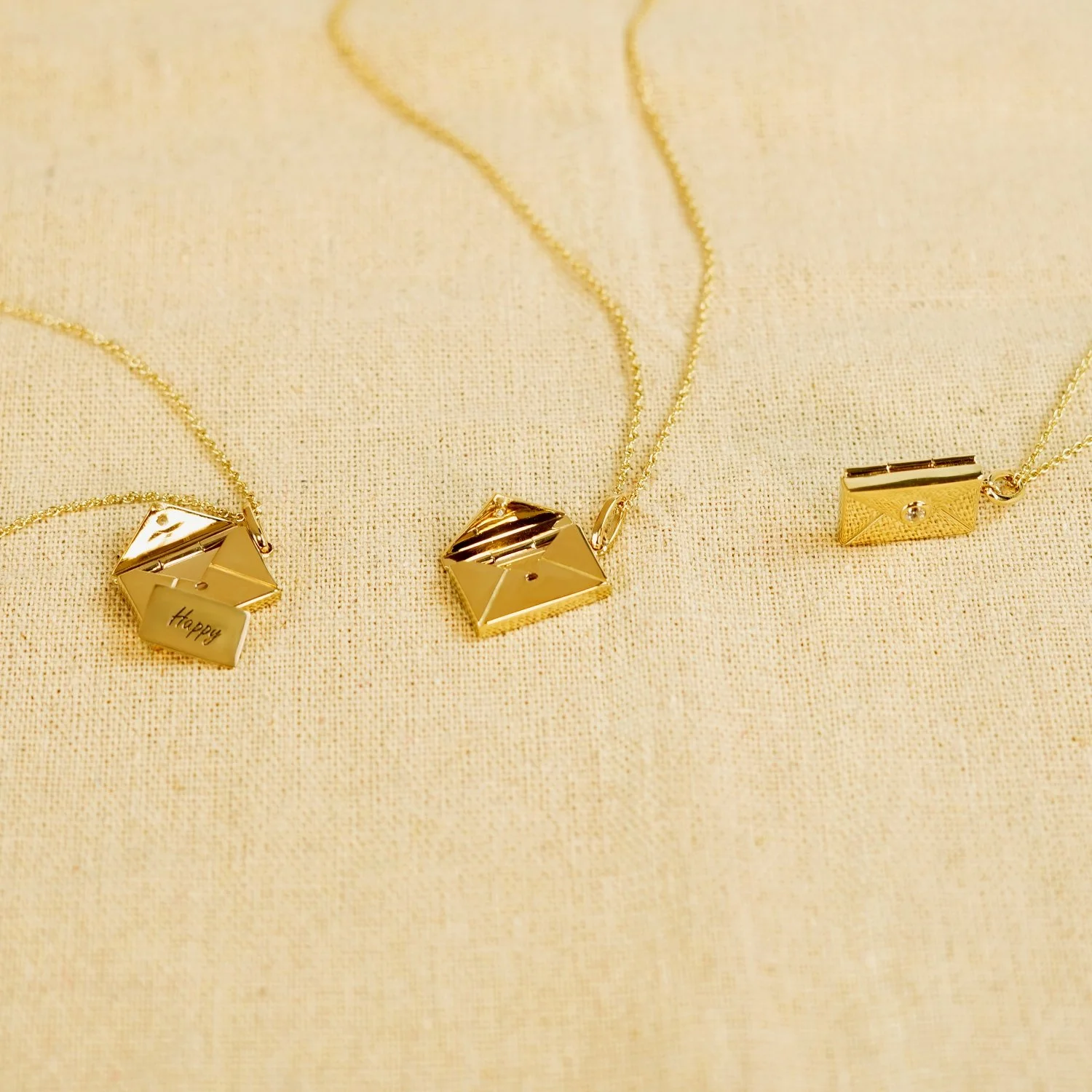 Three gold necklaces with geometric pendants on a beige fabric background.