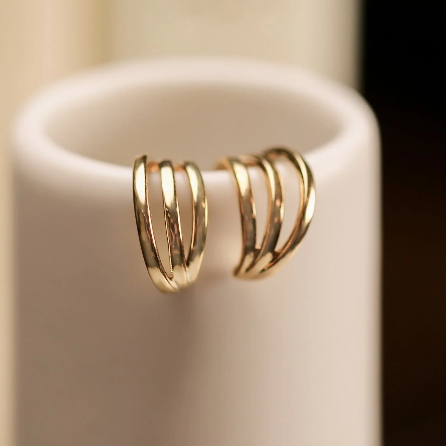 A pair of gold hoop earrings hanging on the edge of a white cylindrical object.
