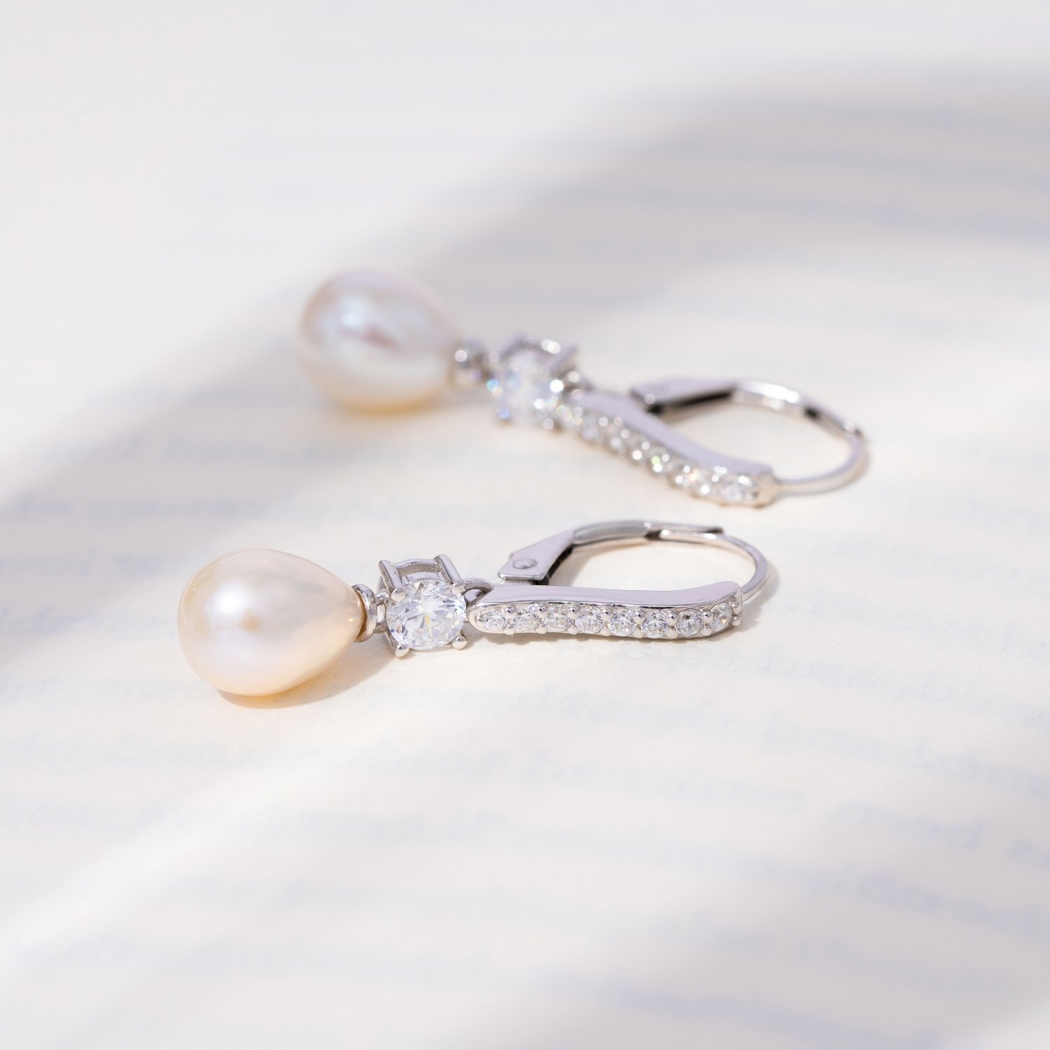 A pair of silver earrings with pearls and diamonds on a light, reflective surface.