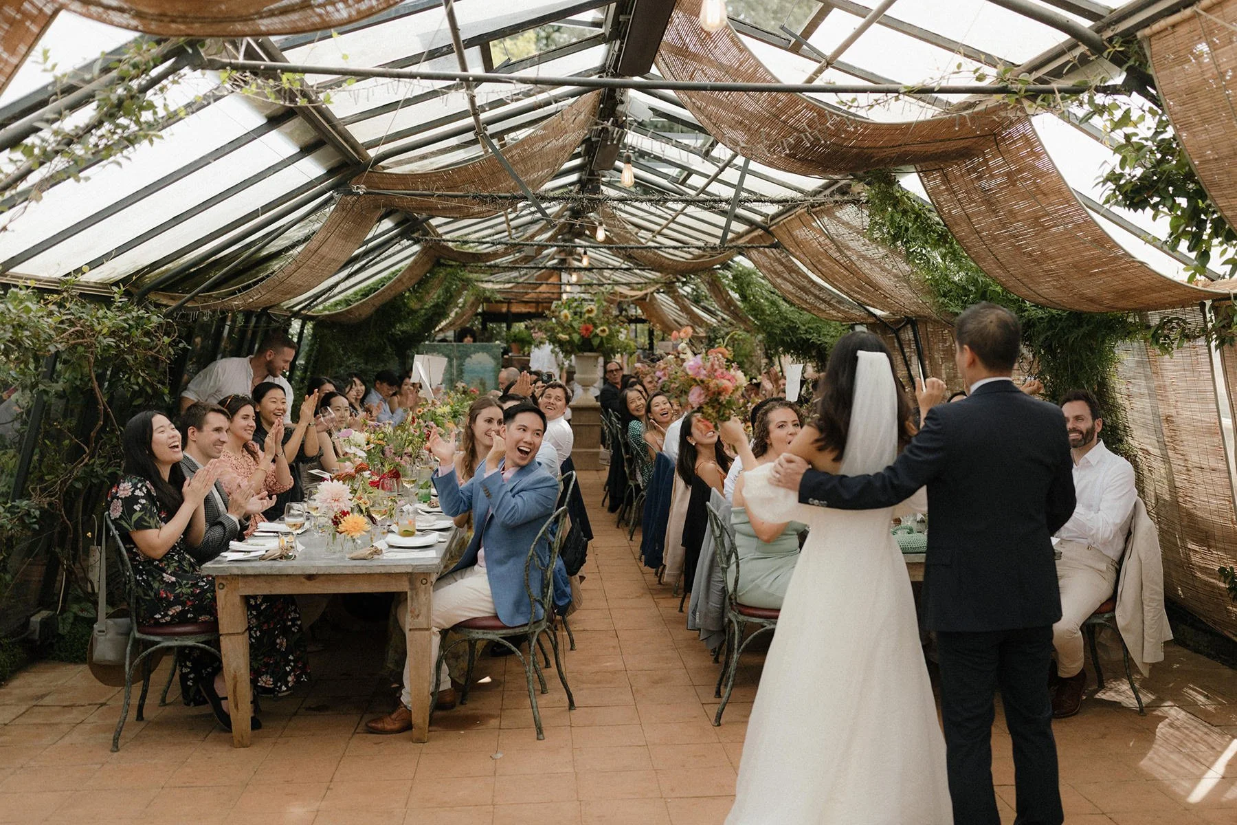 petersham nurseries wedding in richmond, with the couple being announced into wedding breakfast and the crowd cheering in the background 