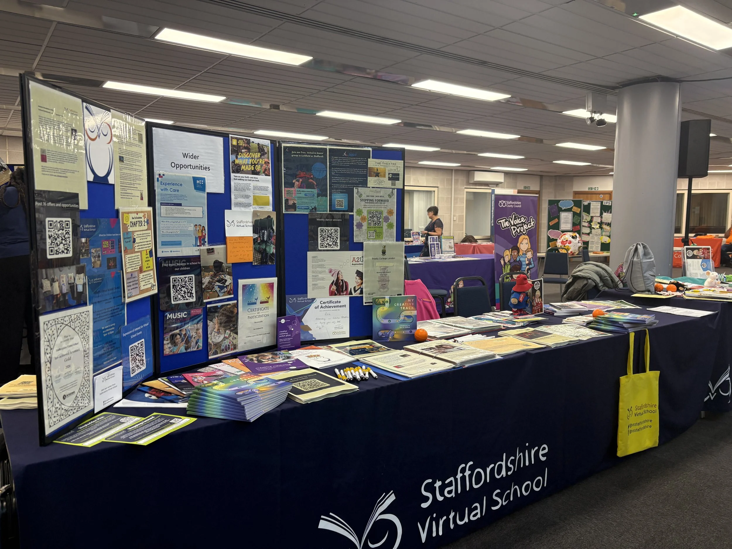Information booth at Staffordshire Virtual School with info boards, pamphlets, and promotional items on a blue tablecloth.