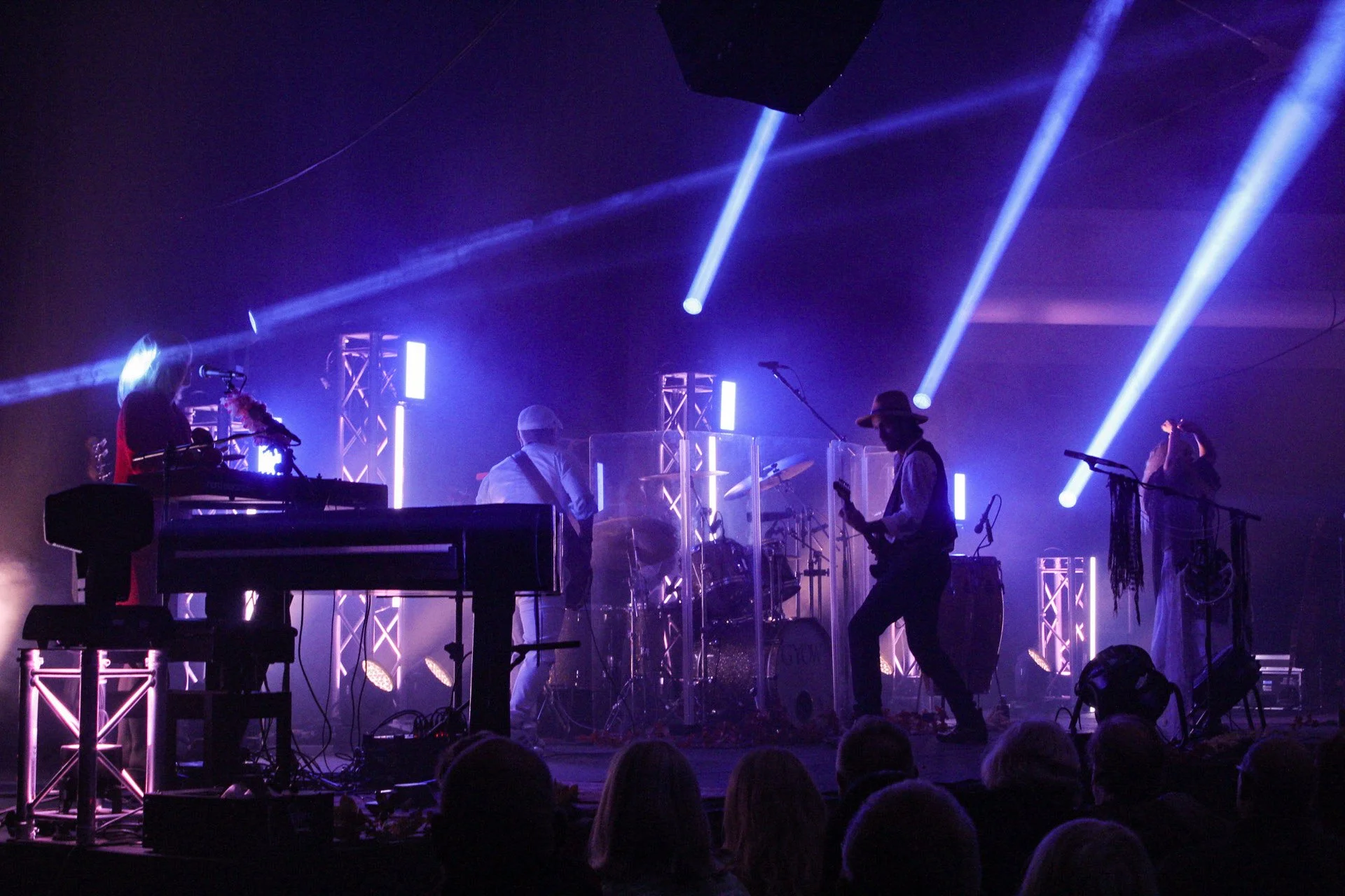 Stage with musicians performing, colorful lights, and audience watching in a darkened theater.