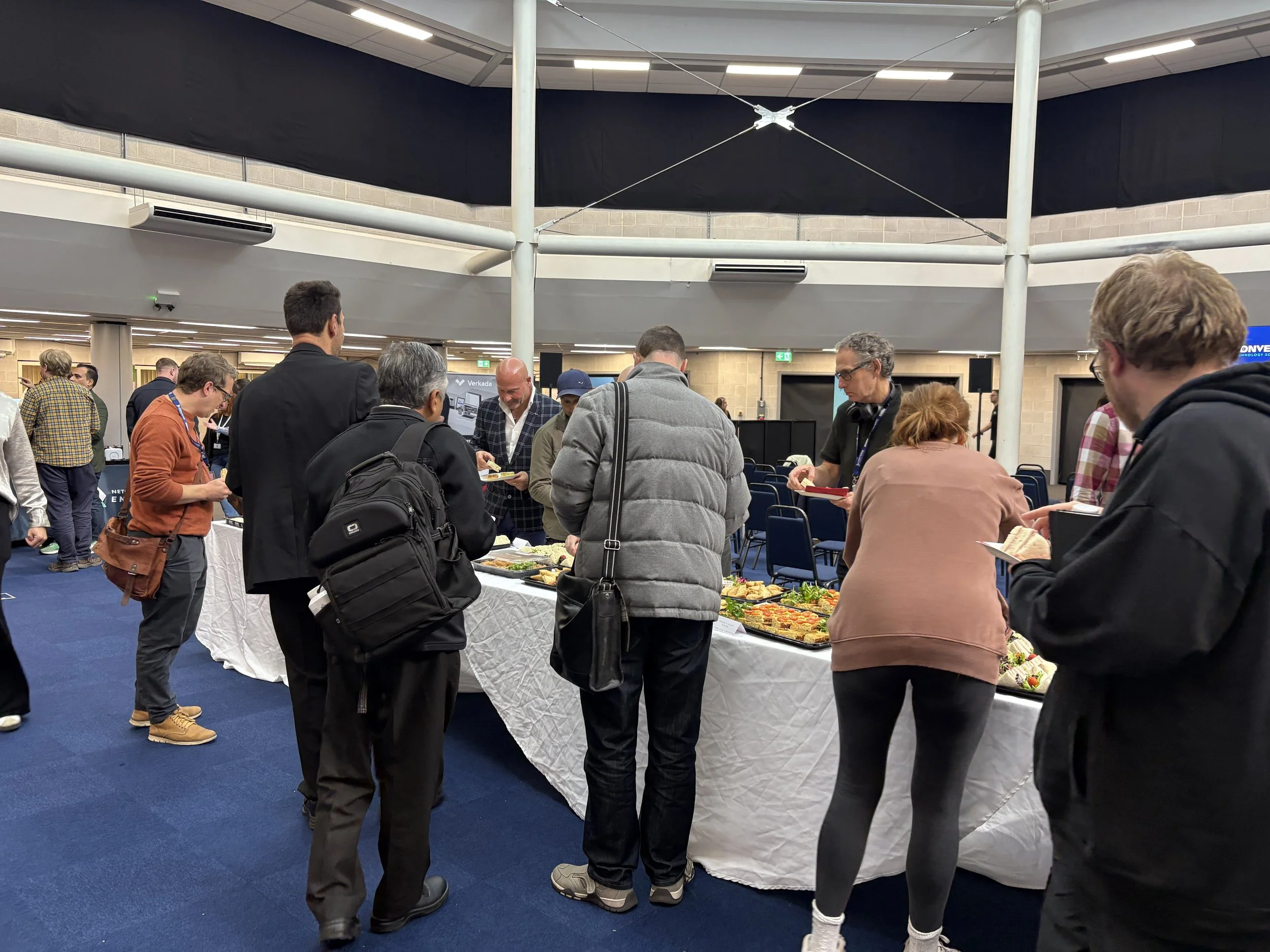 People gathered around a buffet table at a conference, serving themselves food in an indoor event space.