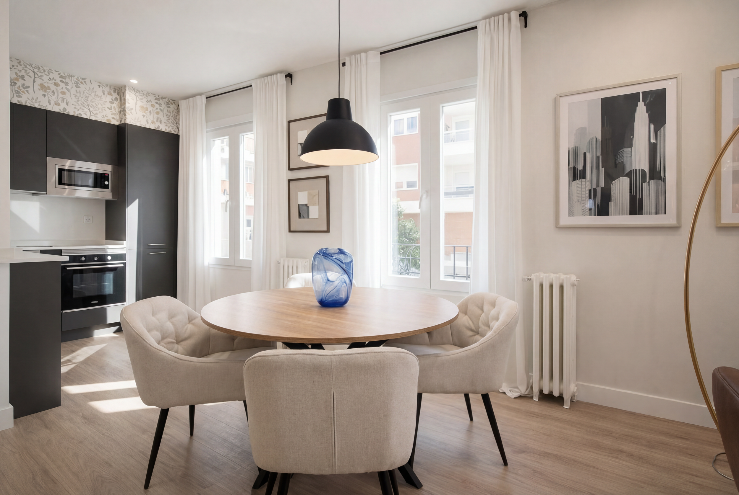 Render_a_House_A_modern_dining_area_with_a_round_wooden_table_and_upholstered_chairs,_adjacent_to_a_sleek_dark_kitchen._Apr_28th.png