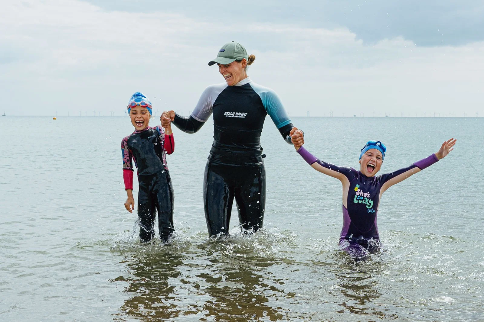 Coach Laura holding hands with two swimmers in the sea, smiling and laughing during a sea swimming lesson in Brighton and Hove
