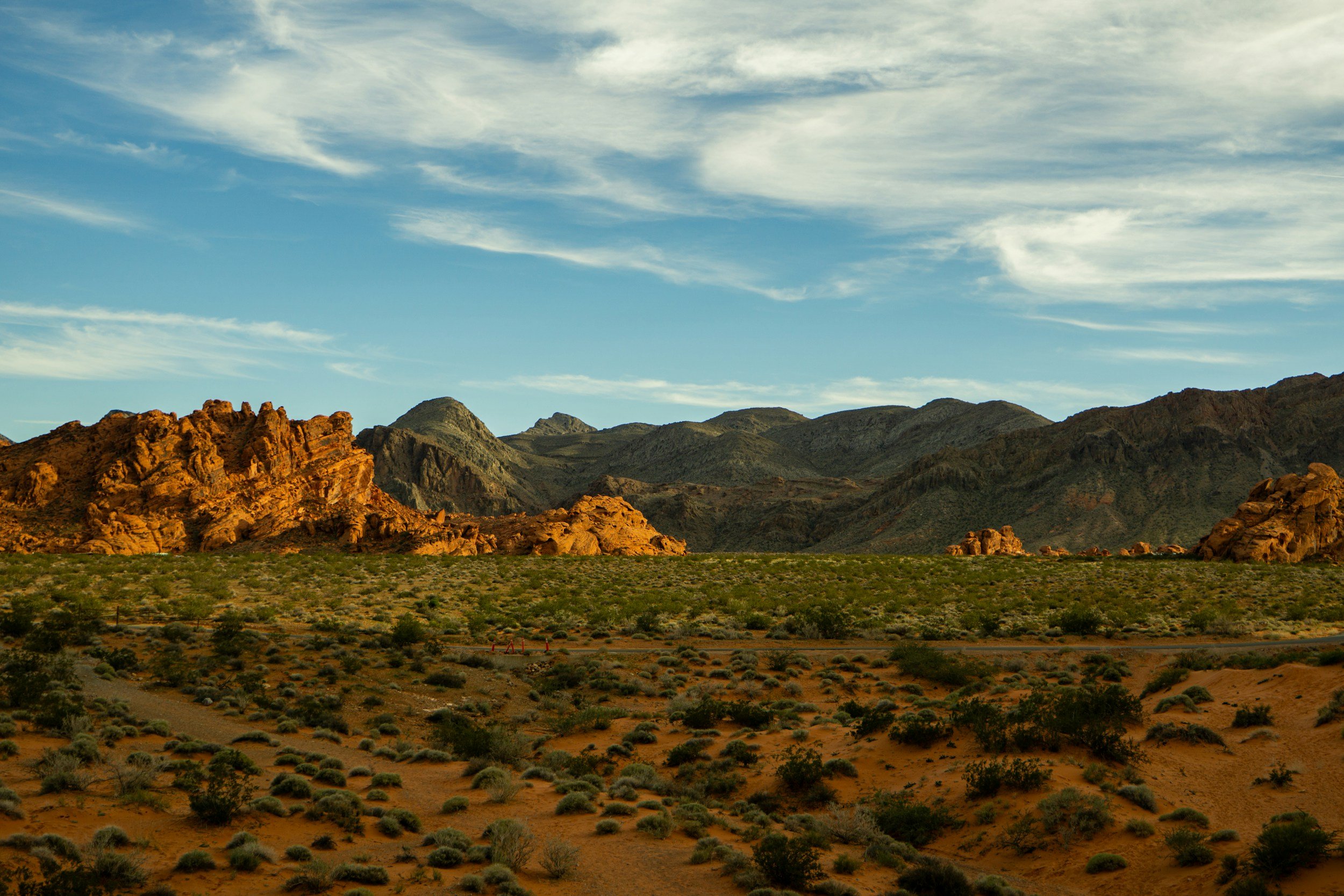 Scenic view of a desert landscape with rocky formations and mountains under a blue sky with scattered clouds.