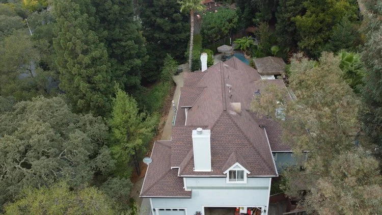 Aerial view of a large house with a brown roof surrounded by dense green trees and vegetation.