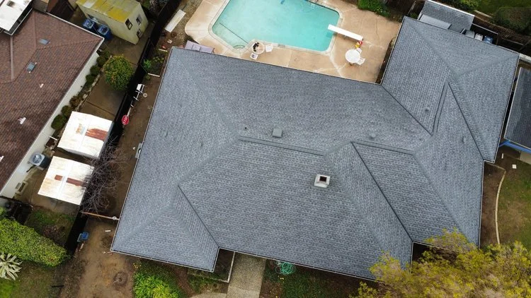 Aerial view of a house with a gray roof next to a swimming pool in a backyard setting.