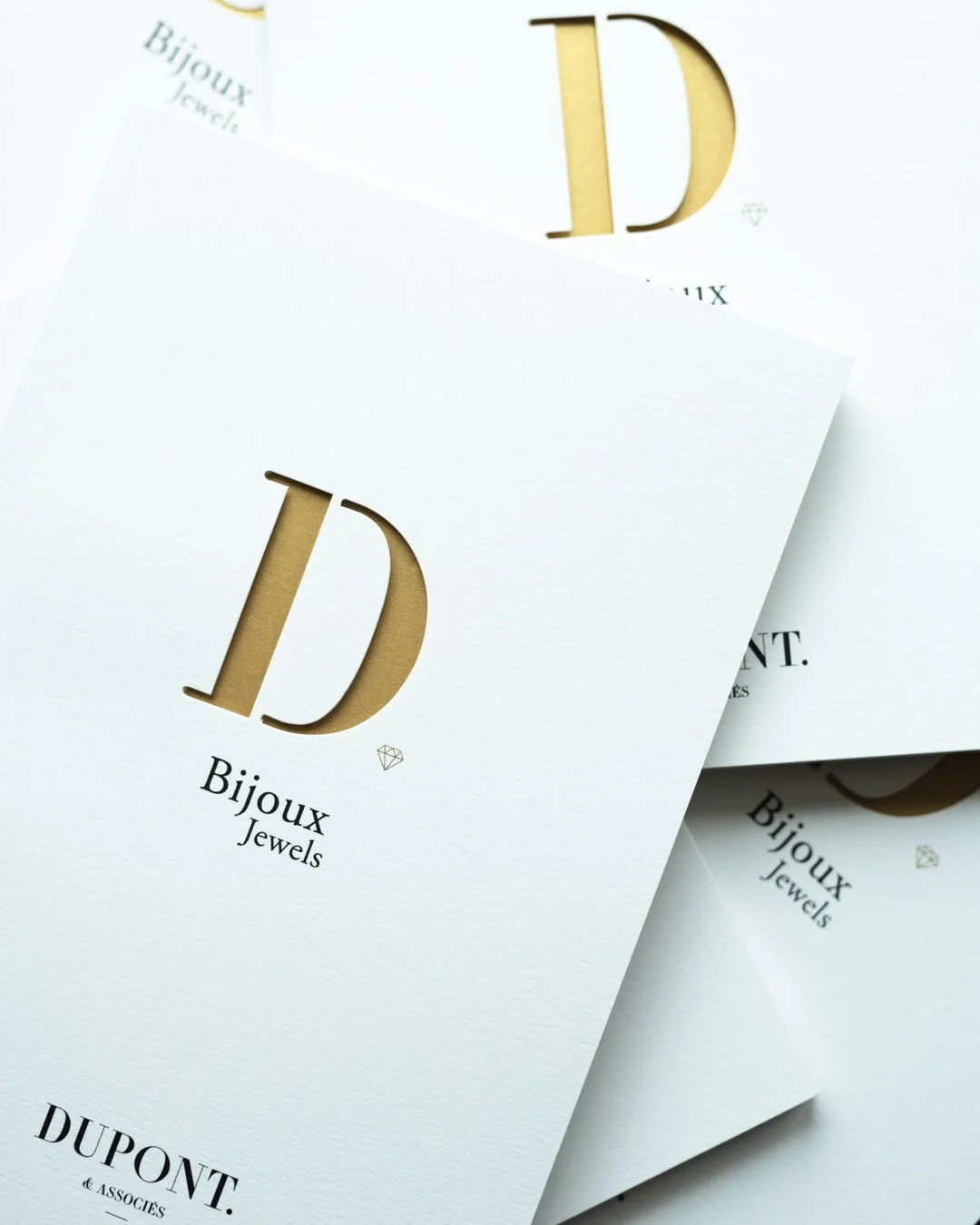 Cartes de visite blanches avec des lettres dorées "D", mention "Bijoux" et "DUPONT & Associés". Design élégant et minimaliste.
