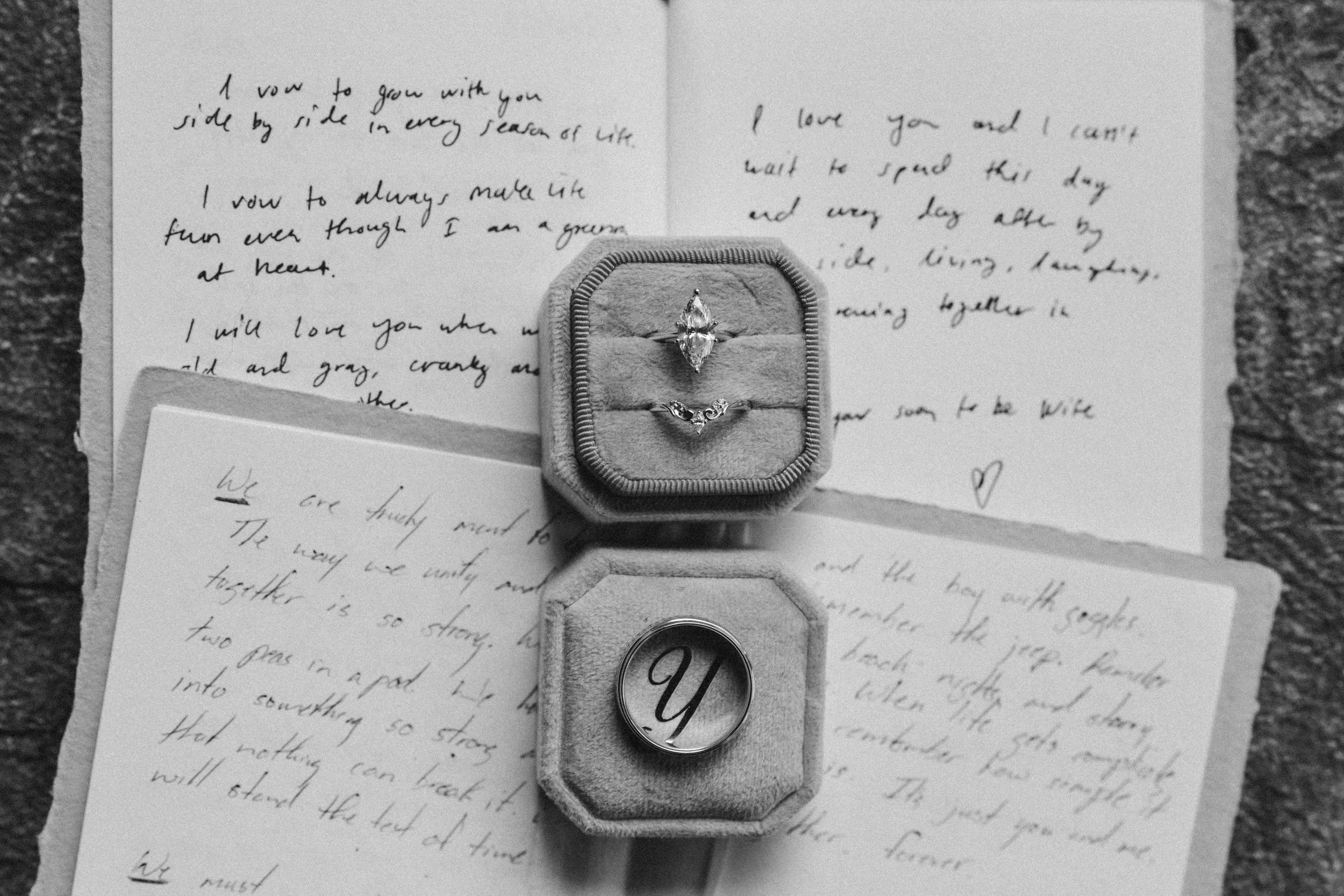 A jewelry ring box containing two rings, one with a large central diamond and the other a smaller band, set on handwritten letters discussing love and commitment.