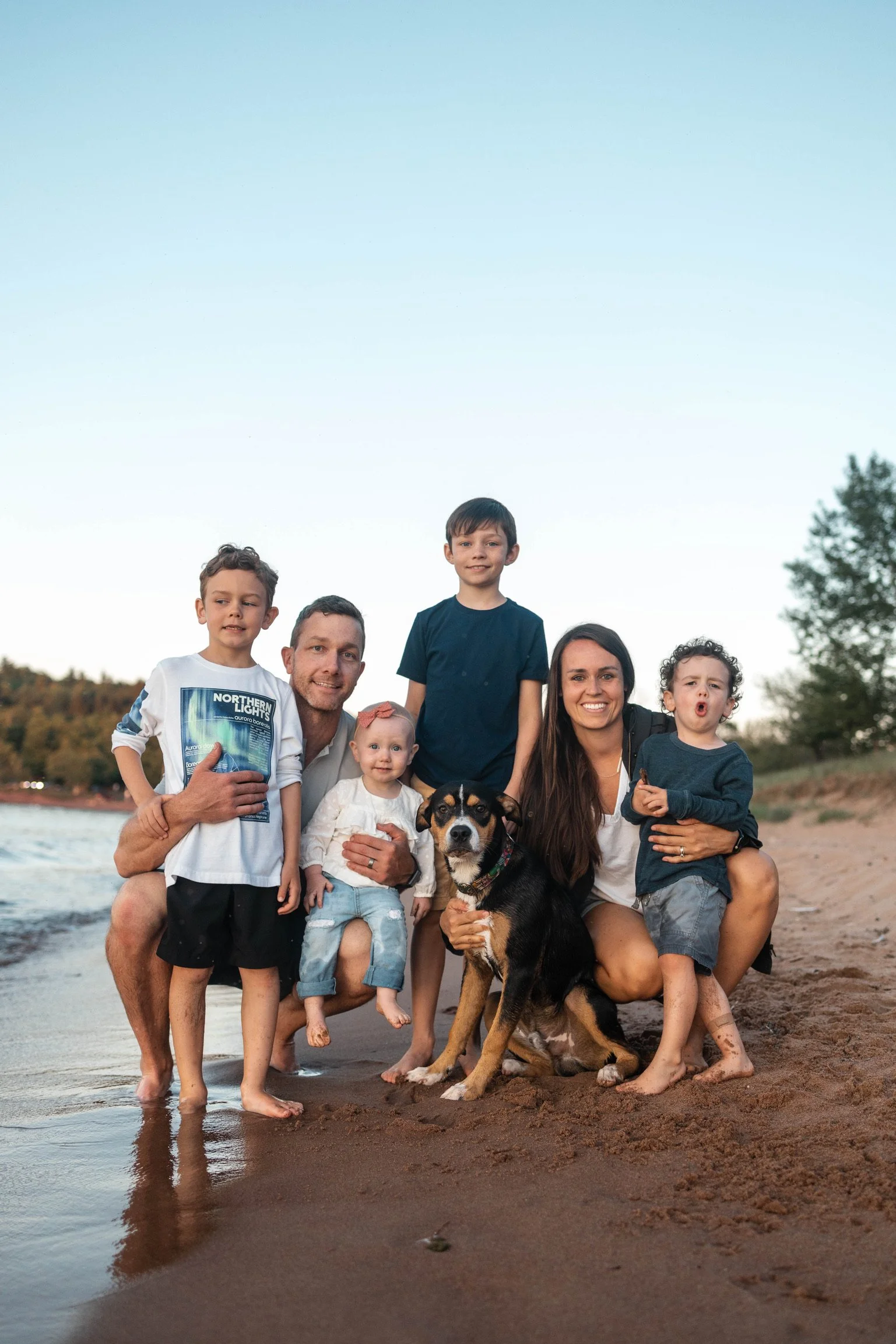 A family of six with a dog on a beach during sunset, smiling and posing for a photo.