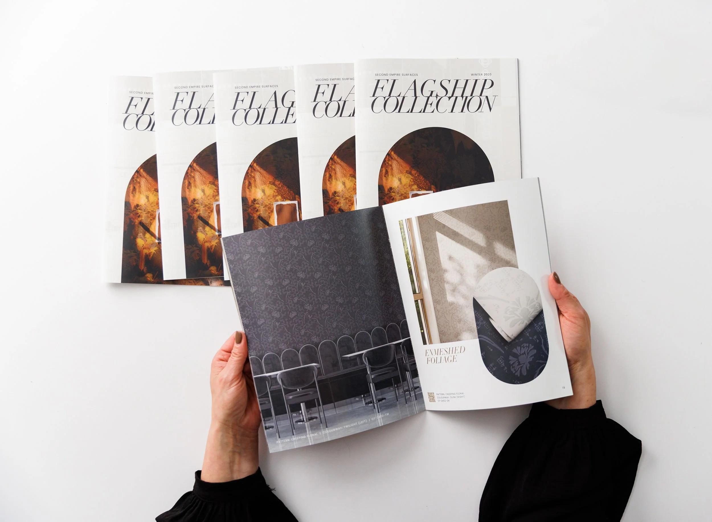 Hands holding and flipping through a catalog with pages displaying Second Empire wallcoverings from the Flagship Collection.