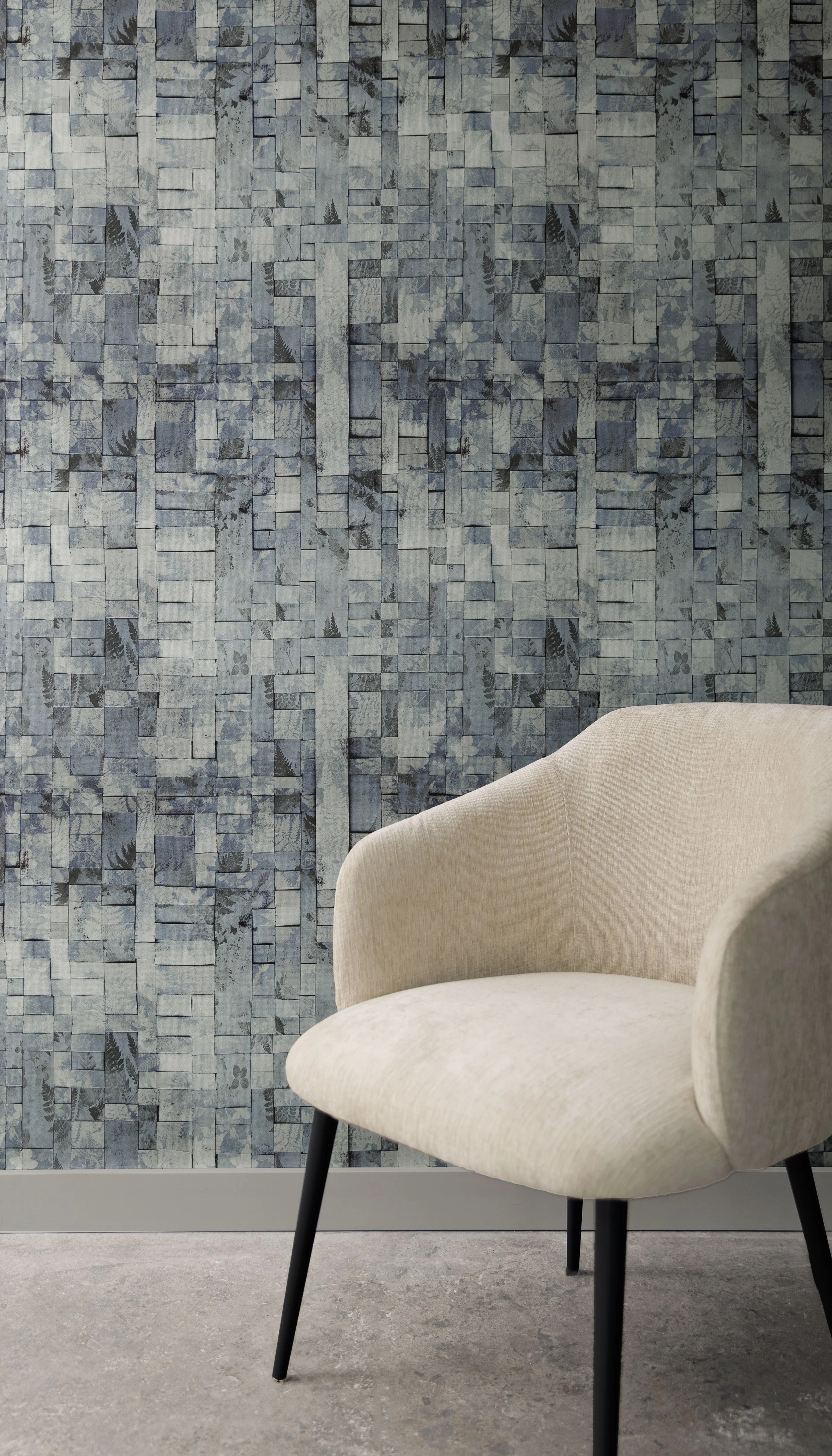 A beige chair set in front of a wall covered with a grey-blue woven wallpaper.