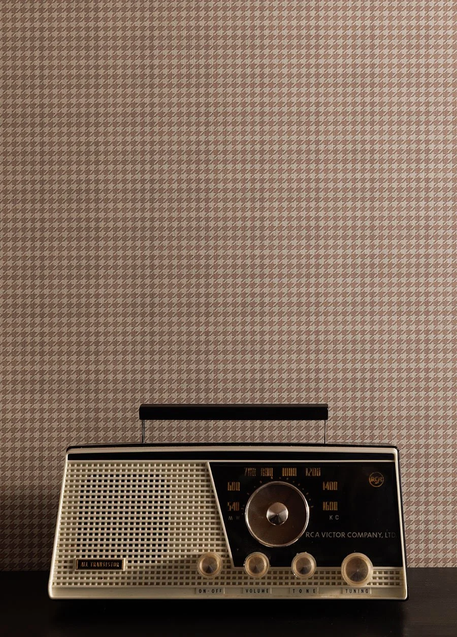 A vintage radio with a black and white design, featuring a large tuning dial, volume and tone controls, and a speaker grille, placed on a black surface against a houndstooth patterned wallpaper in a cream color.