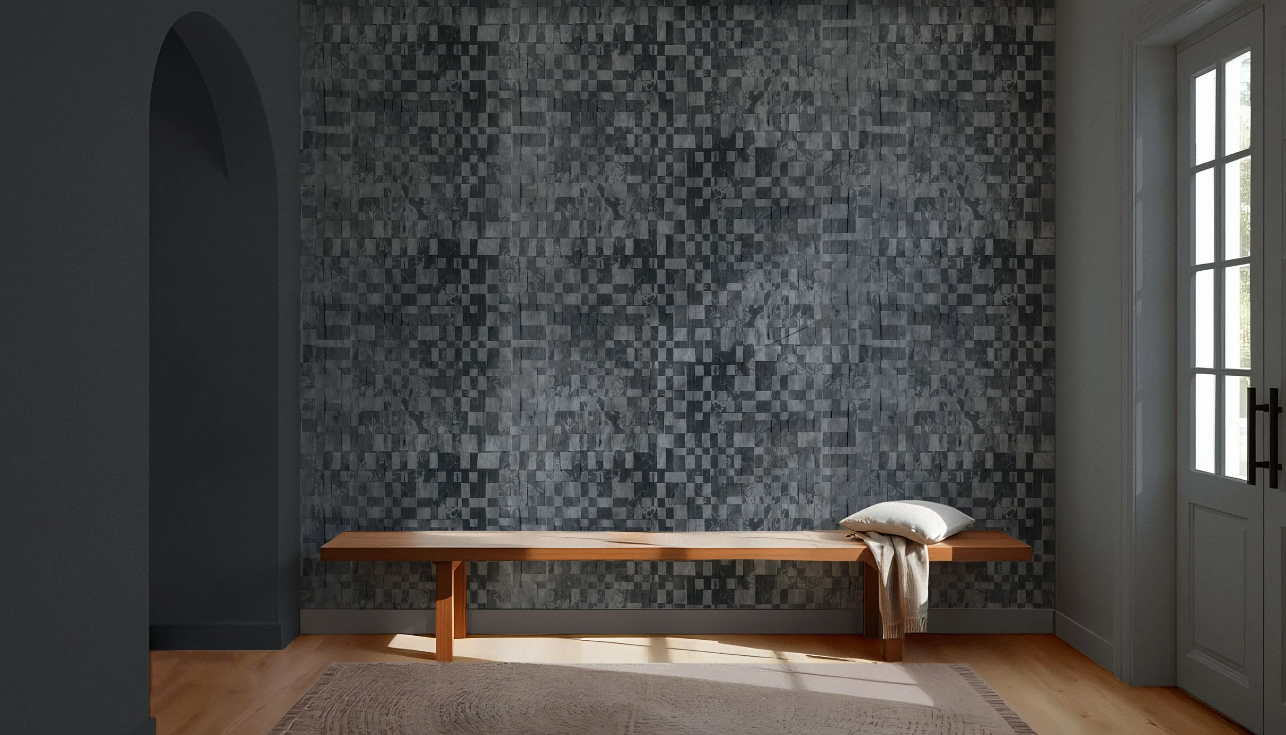 A bench with a blanket and cushion on one end in front of a wall with deep blue wallpaper featuring a woven design.