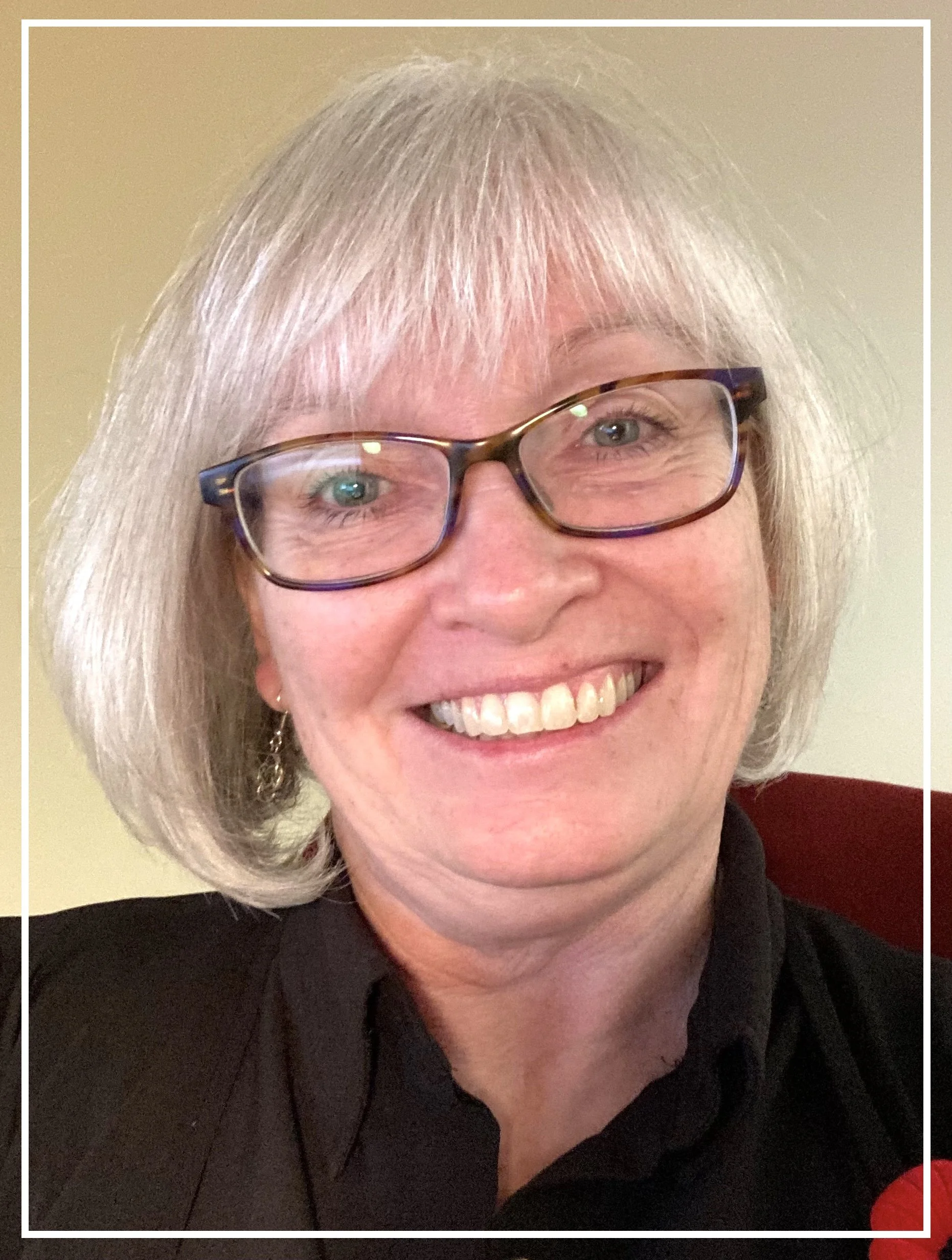 Michele, smiling and wearing glasses, with short grey hair.