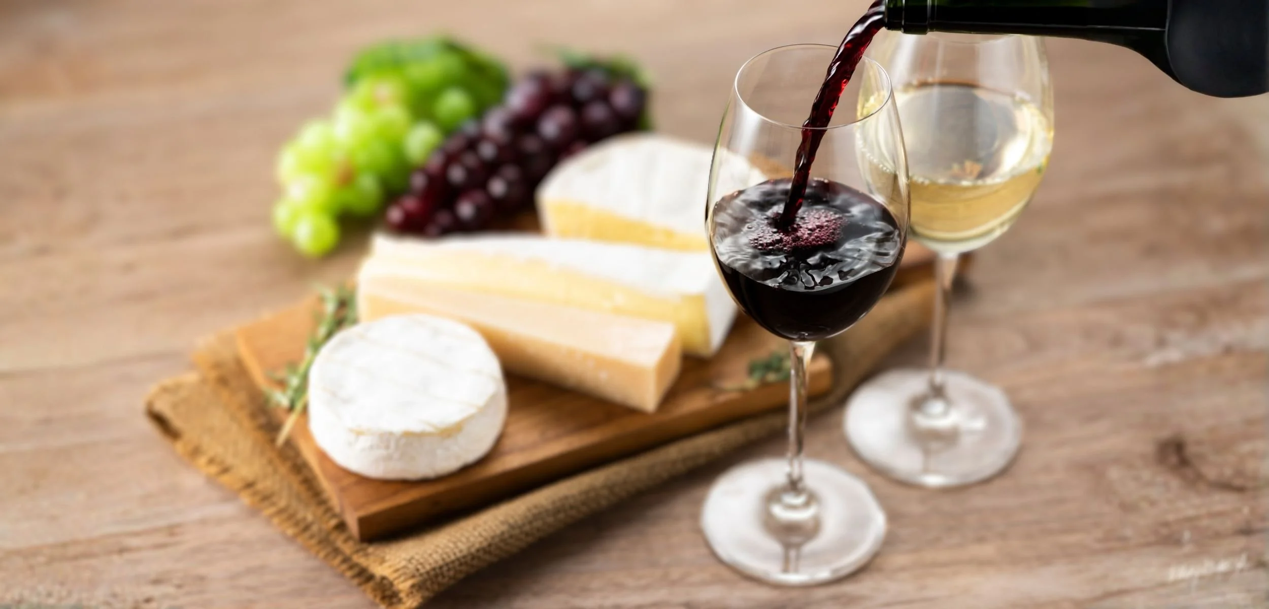 A selection of cheeses paired with non-alcoholic red and white wine, grapes, and a wooden serving board, ideal for a gourmet tasting experience.