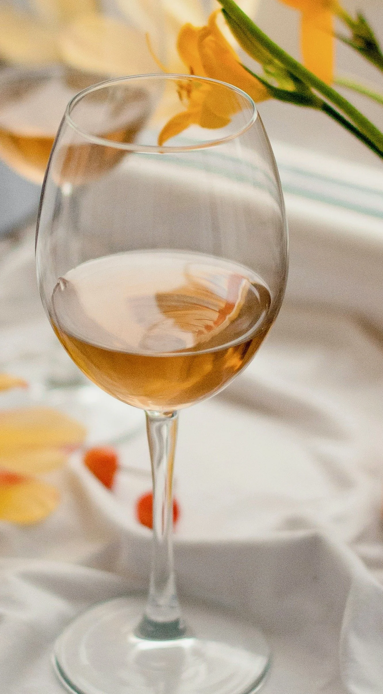 Glass of non-alcoholic white wine on a white tablecloth with yellow flowers in the background